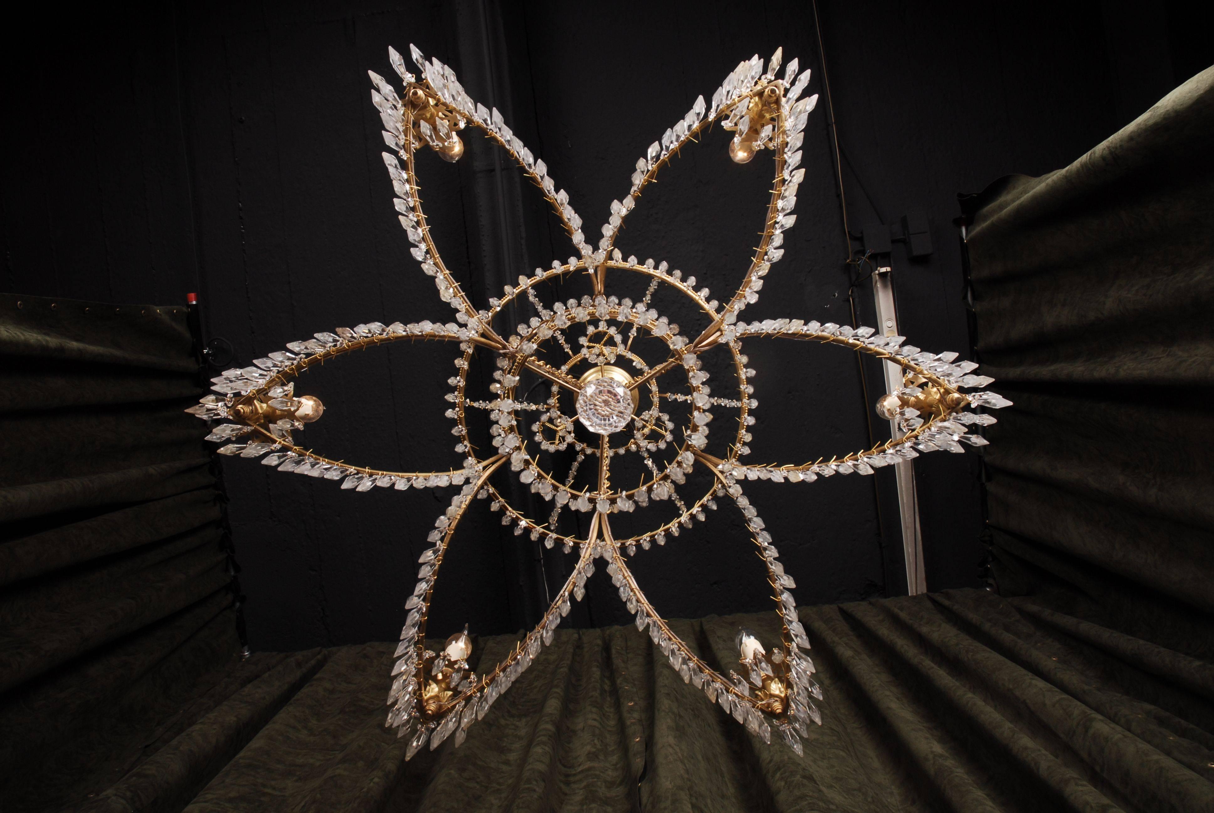 Splendid classicist Swedish ceiling candelabra.
Polished brass. Sweeping, star fomed body with drop-forming, facetted glass. There from, six-light arms ending in eave shells. Above the curved, star-formed chandelier-ring, are two juvenescent hoops