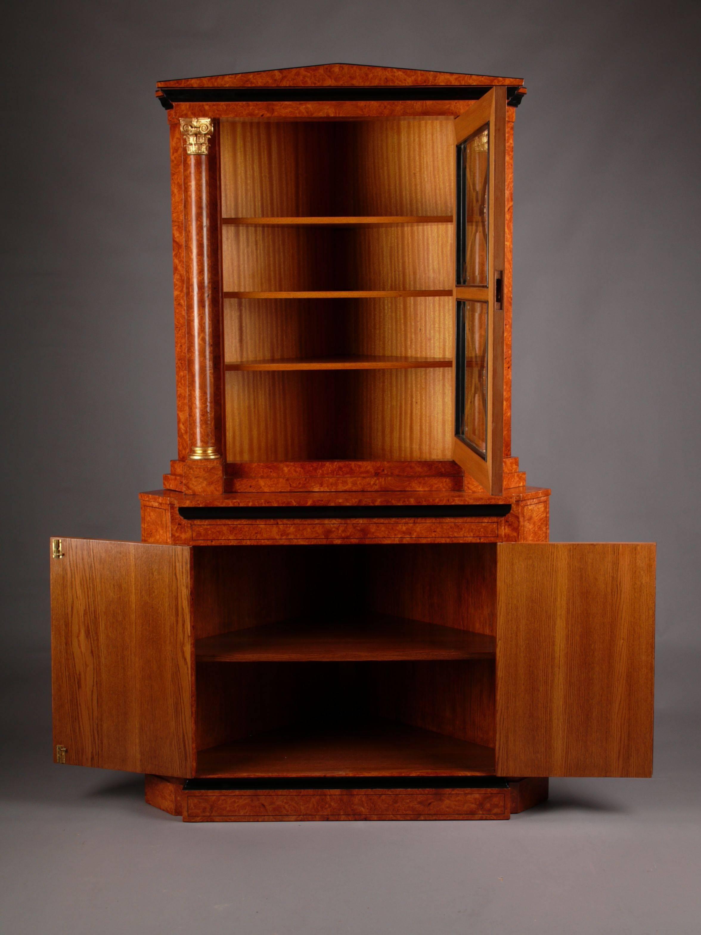 Elegant corner cupboard in Biedermeier style.
Bird’s eye maple root veneer on solid pinewood. Partially ebonized. Two drawered body over prominent overhanging pedestal, internal shelves. Narrow over hanging top platter. Over which a one drawered