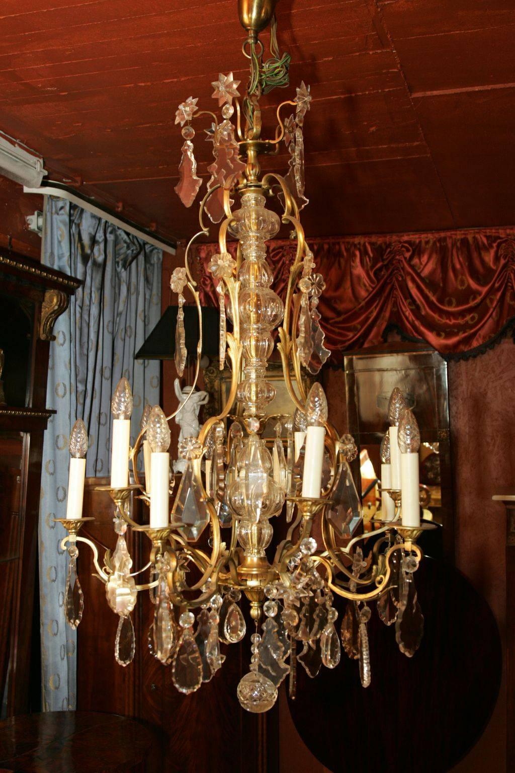 Antique French chandelier of the 18th century.
Frequently curled basket rods. In the center rising, multi-articulated baluster-shaped glass shaft with multiple crowns. Brass, chiselled. High baluster-shaped body with ten externally mounted flames.