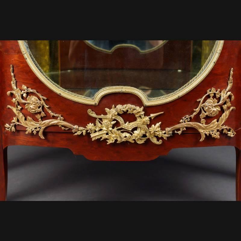 Majestic French Vitirne Napoleon III in transition style Paris.
Rich in extremely finely chiselled, fire-gilt decorative bronze fittings.
Mahogany on solid softwood. High-angled, one-door, cambered and three-sided glazed body on tall, slanting,