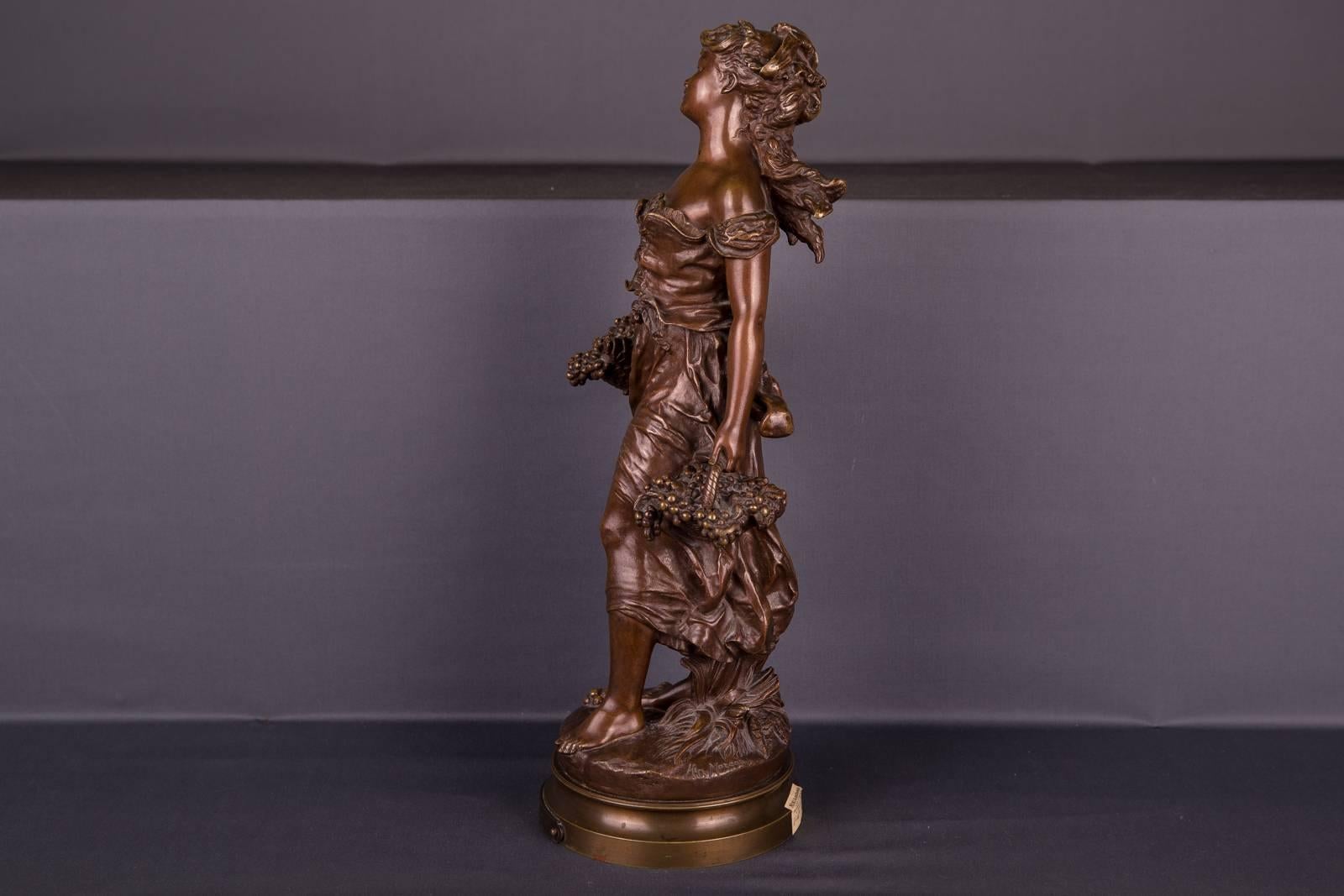 Große Bronzeskulptur des Künstlers Moreau, die eine junge Dame im Sommerkleid darstellt. Frei fahrende Dame mit offenem Haar und leicht lächelndem Gesichtsausdruck, die in die Ferne schaut. In jeder Hand hält er einen Korb mit vollen Weinblättern,