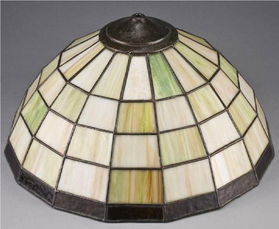 This is a beautiful rare estate Handel stained glass lamp circa 1910 with leaded panes joining green and beige slag glass panels, bordered at the bottom with textured amber panels; raised on a copper patinated base. Stamped 