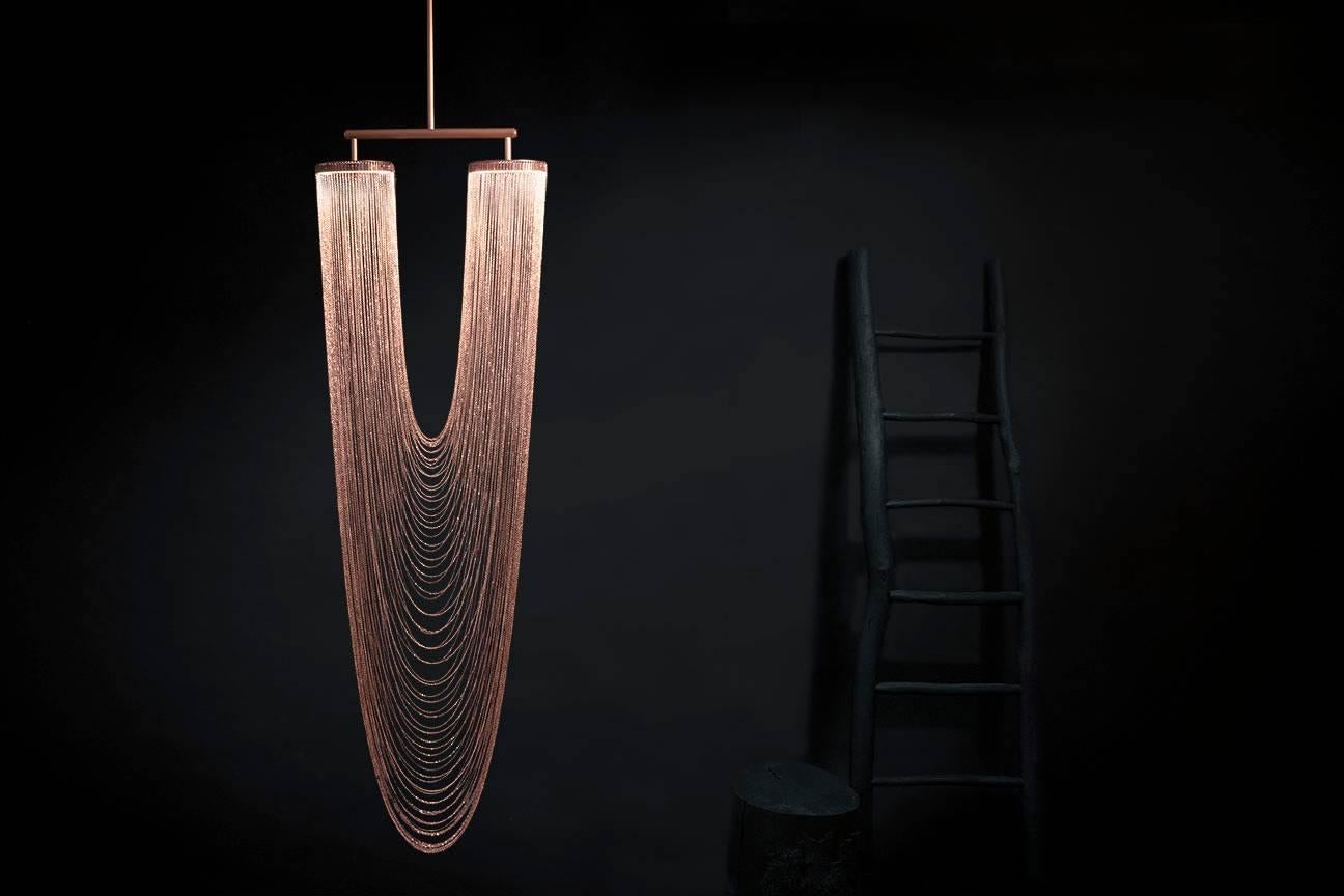Otero is a luxurious high-end lighting fixture that has been coated with warmth and elegance. This sculptural light is handcrafted with delicate copper chains to create a unique and elegant curved shape inspired by the romantic world of jewelry. The