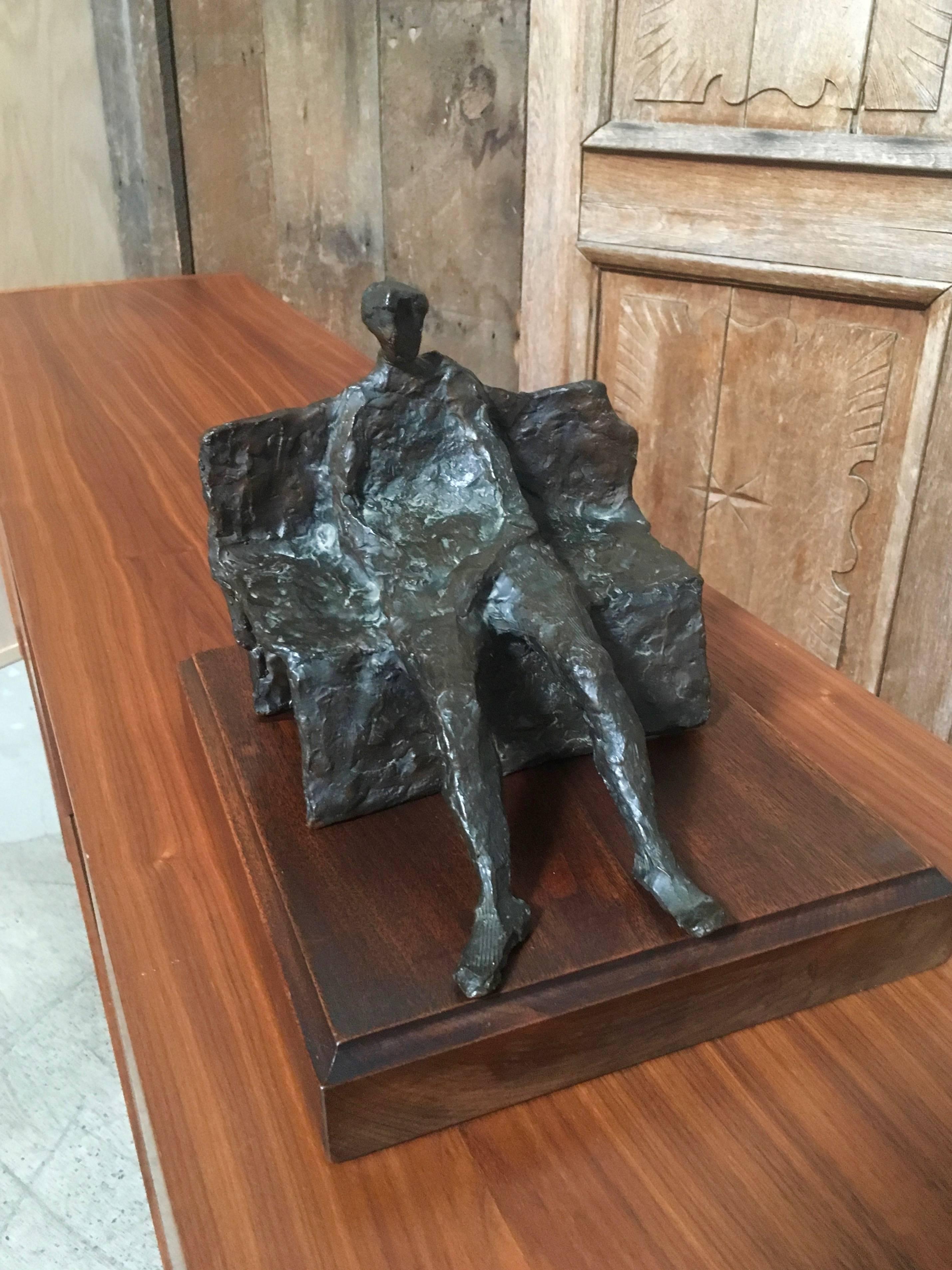 Anonymous bronze sculpture of a man sitting on a bench on a walnut platform.