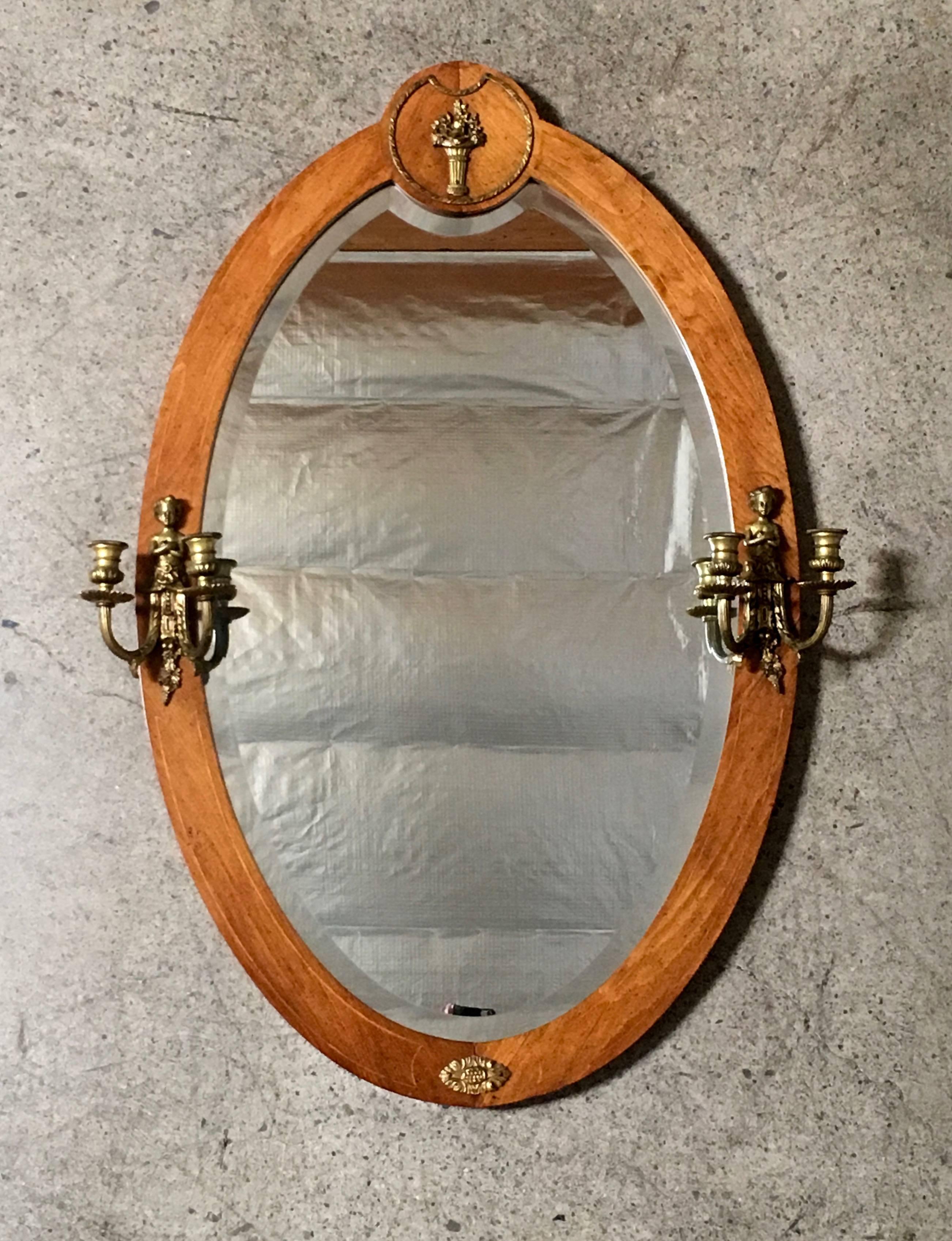Oval beveled mirror with inlaid wood frame and brass sconces. This can be used with candles or converted to electric.