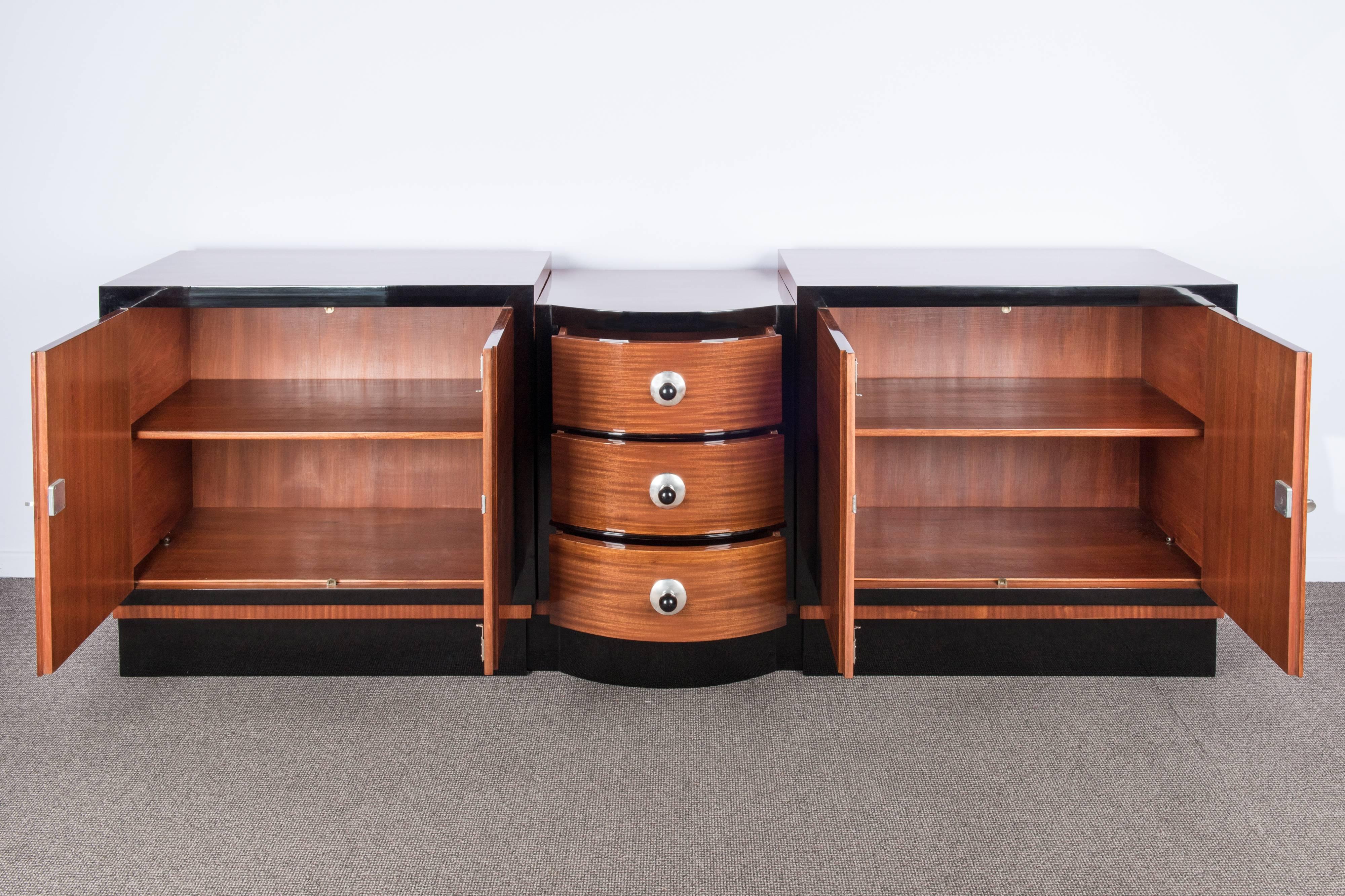 Spectacular mahogany veneered Art Deco sideboard. Two lateral cabinets with doors opening to a space with shelves, three large drawers in the middle.
The frame of the art-deco credenza is black laquered. Keys and hardwares are silver plated, the