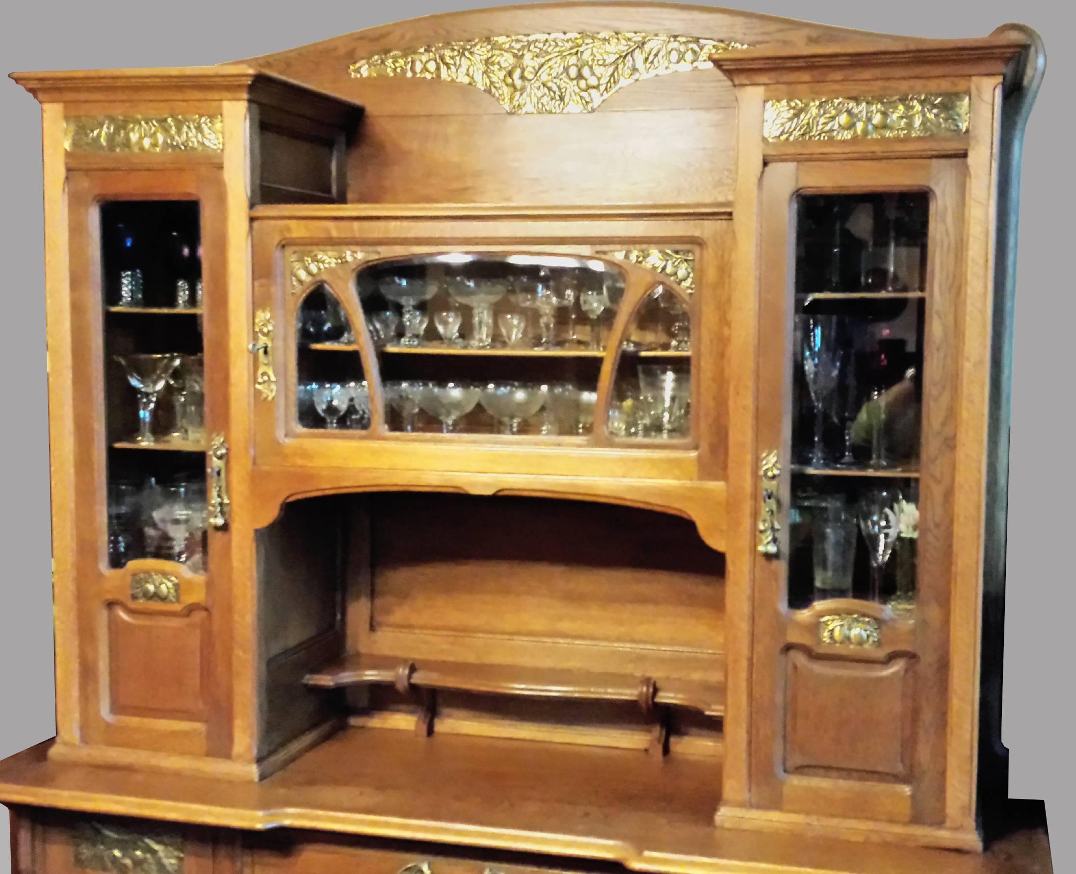 Beautiful and impressive tall Art Nouveau credenza buffet, in two parts, (that can be separated from each other) made in solid oak with gorgeous stamped brass decorations in the shape of cherries in many parts of it.
Gorgeous handles and locks in