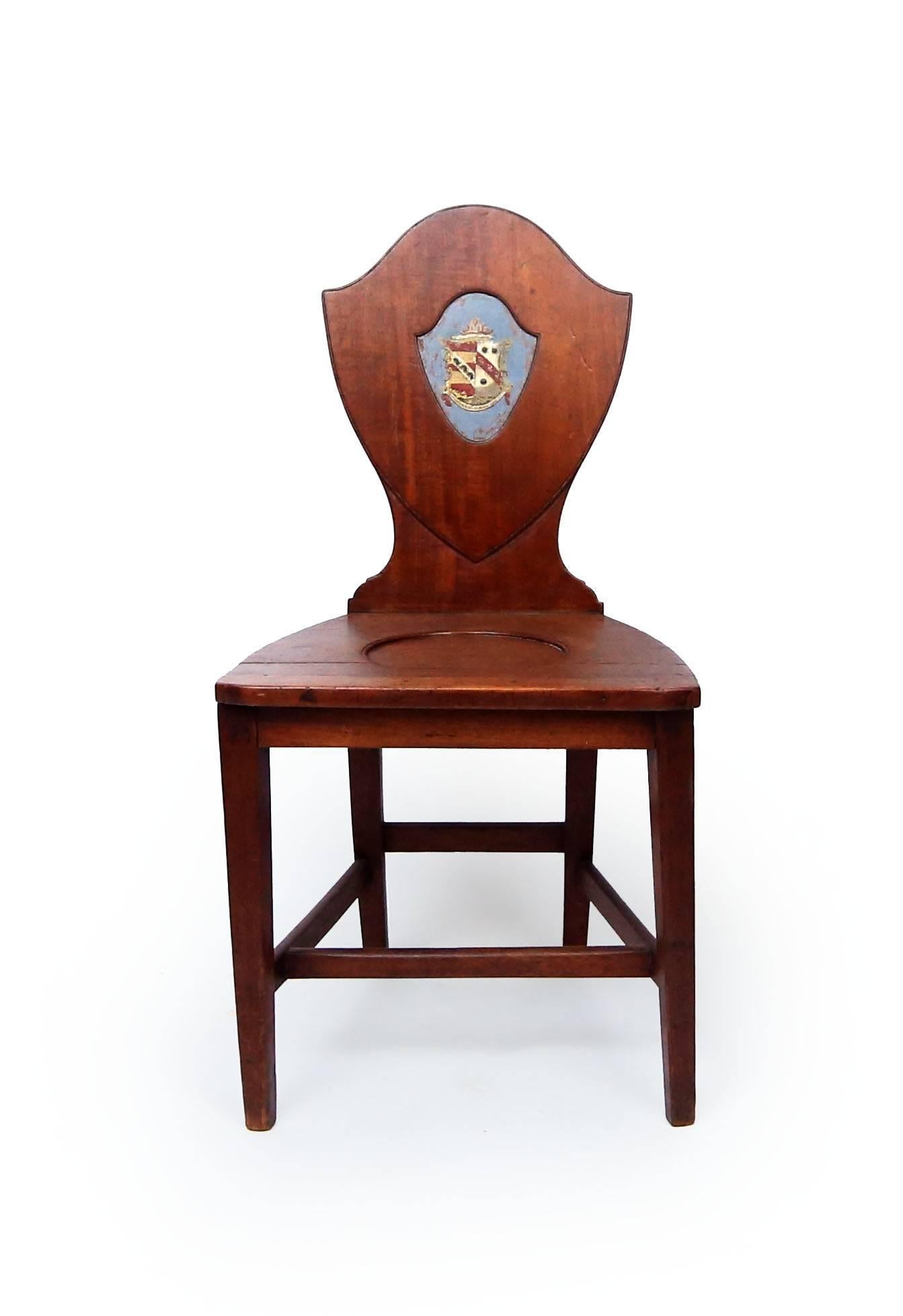 Fine George III mahogany hall chair, the shield back bear painted heraldic crests commemorating the union of the original owners: one half lions rampant and the other swans. The banner below reads 