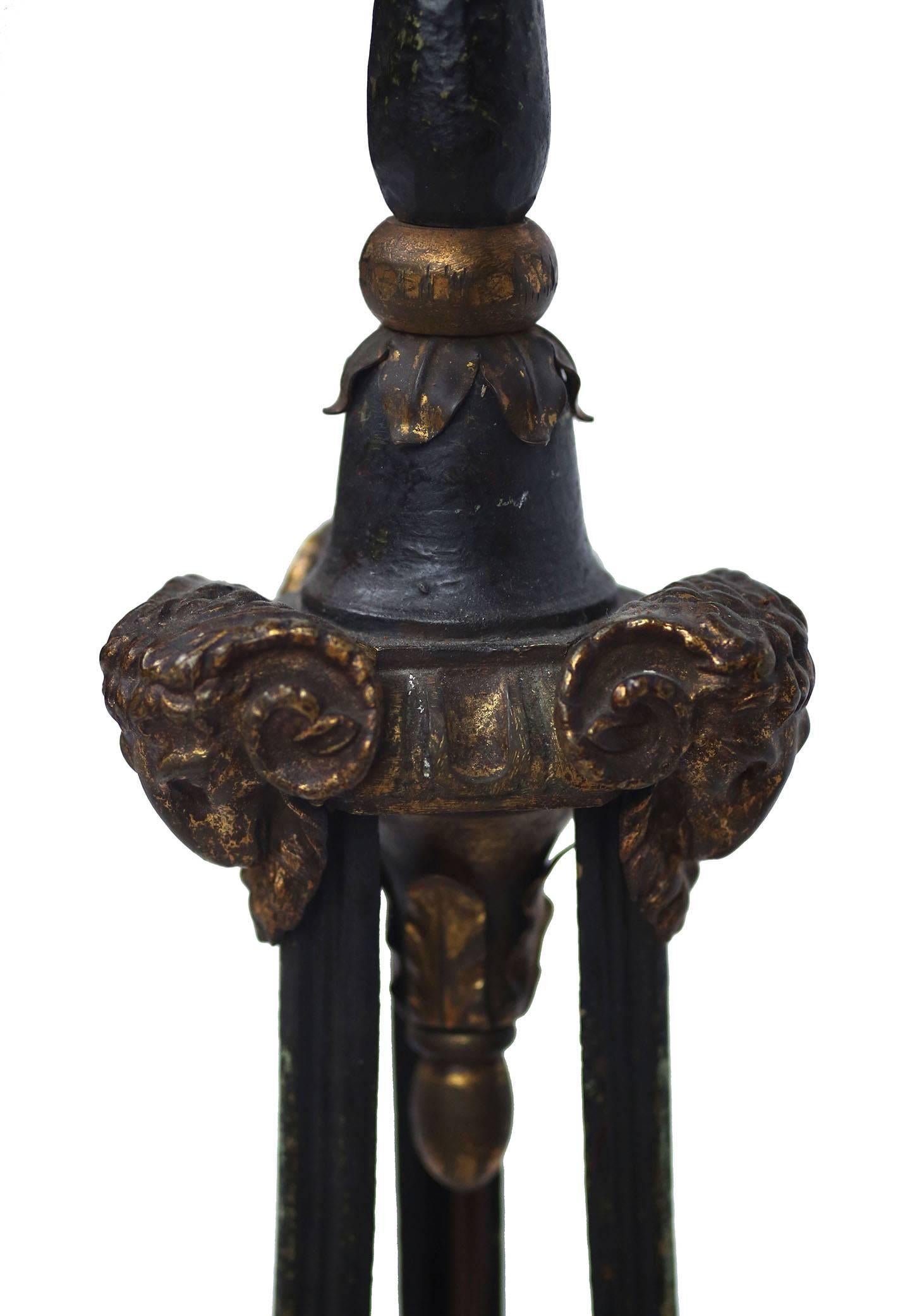 French iron floor lap with tripod base terminating in brass cloven hooves. The upper base is decorated with brass rams heads and foliate turned details. The lamp is painted with a fine verdigris finish and ruby fleck. Offered with a light cream