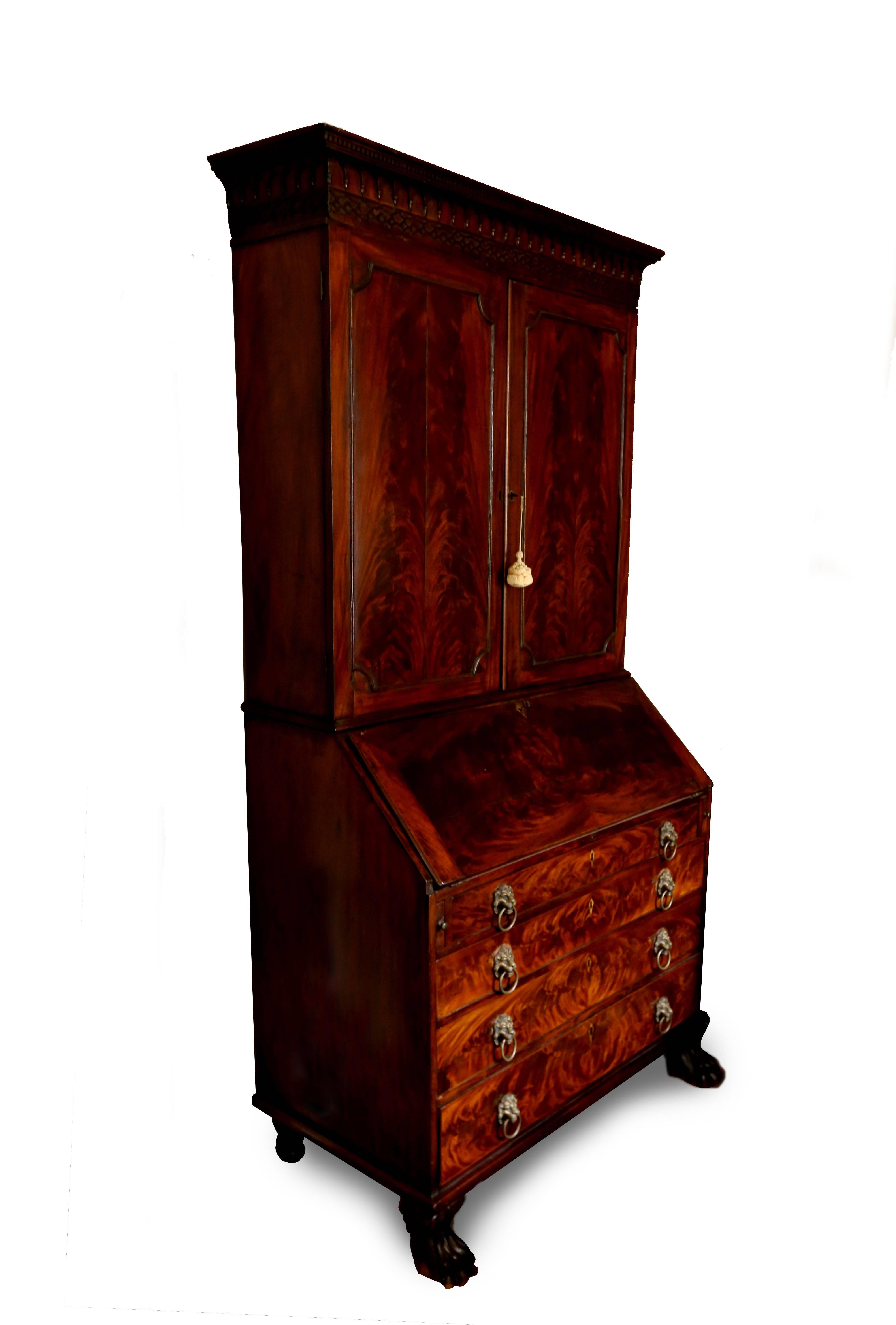 Magnificent flame mahogany secretary. The cornice of the piece features fine dentils, gothic arches, and delicate blind fretwork. The upper two doors of paired veneer open to sets of original shelves with adjustable supports. The matchbook veneer