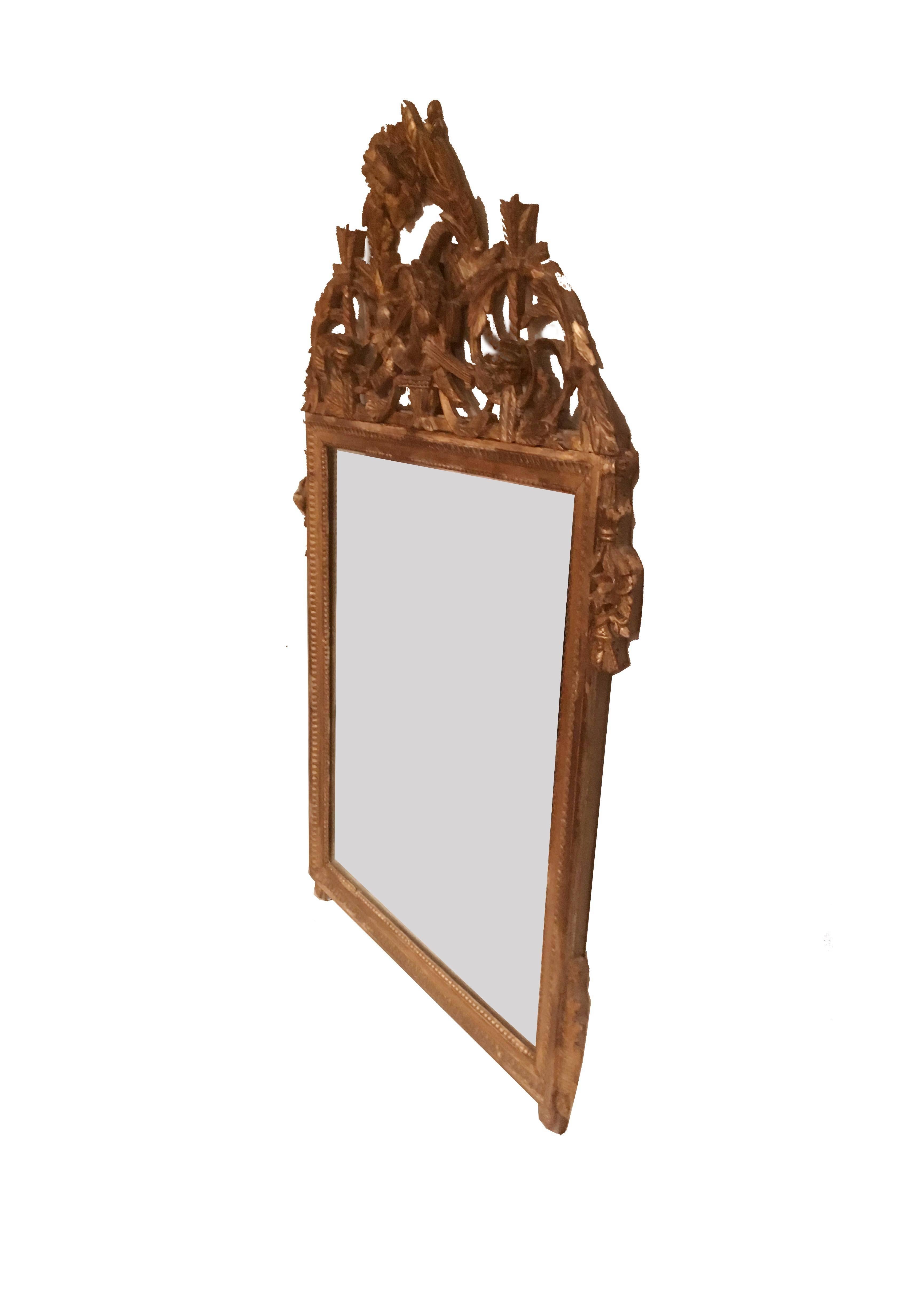Late 18th century Louis XVI French gilt mirror with elaborate crown. The frame exhibits lambs tongue and beading detail while the surmount contains laurel wreaths, lyres, garlands and swags. A fine classical mirror with 19th century patinated glass.