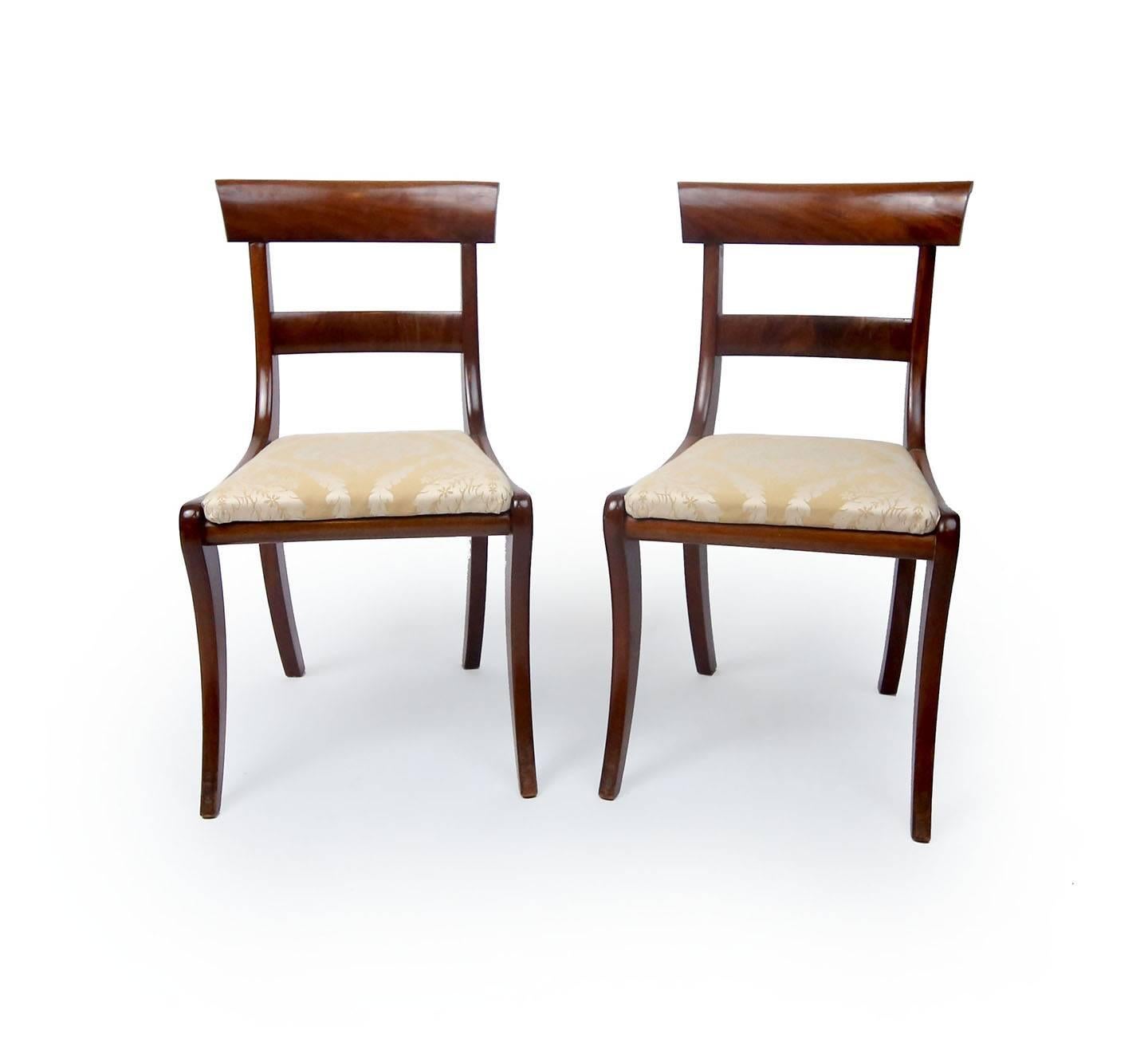 Two handsome mahogany chairs, with molded crest rail, saber legs and Classic Klismos shape. Upholstered in a gold and cream damask, England, early 20th century.