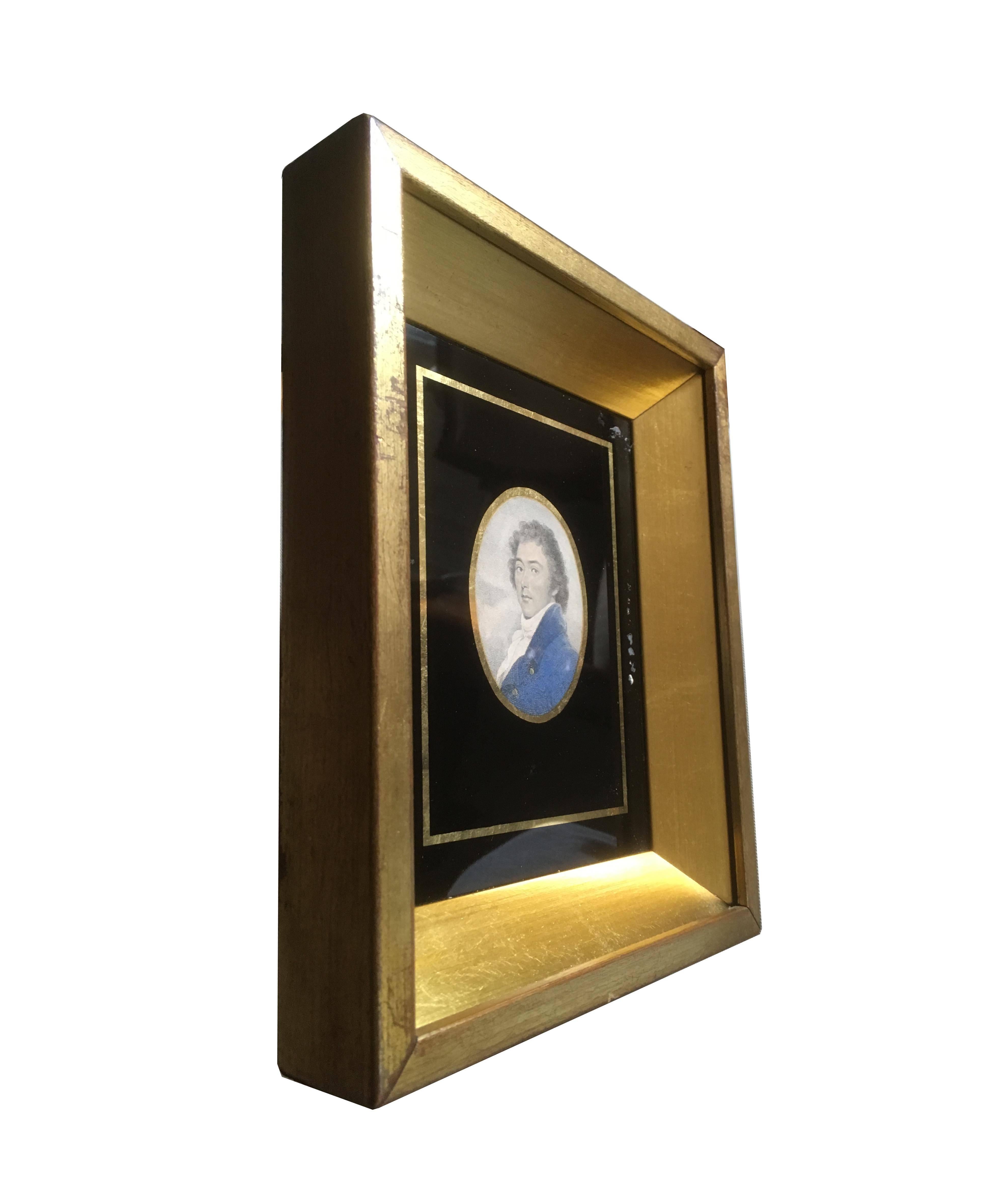 A fine portrait miniature of a man with long tousled hair and blue high-collared frock coat. The image is encased by parcel-gilt and black lacquered glass with a thick giltwood shadowbox frame, Continental Europe, circa 1815.