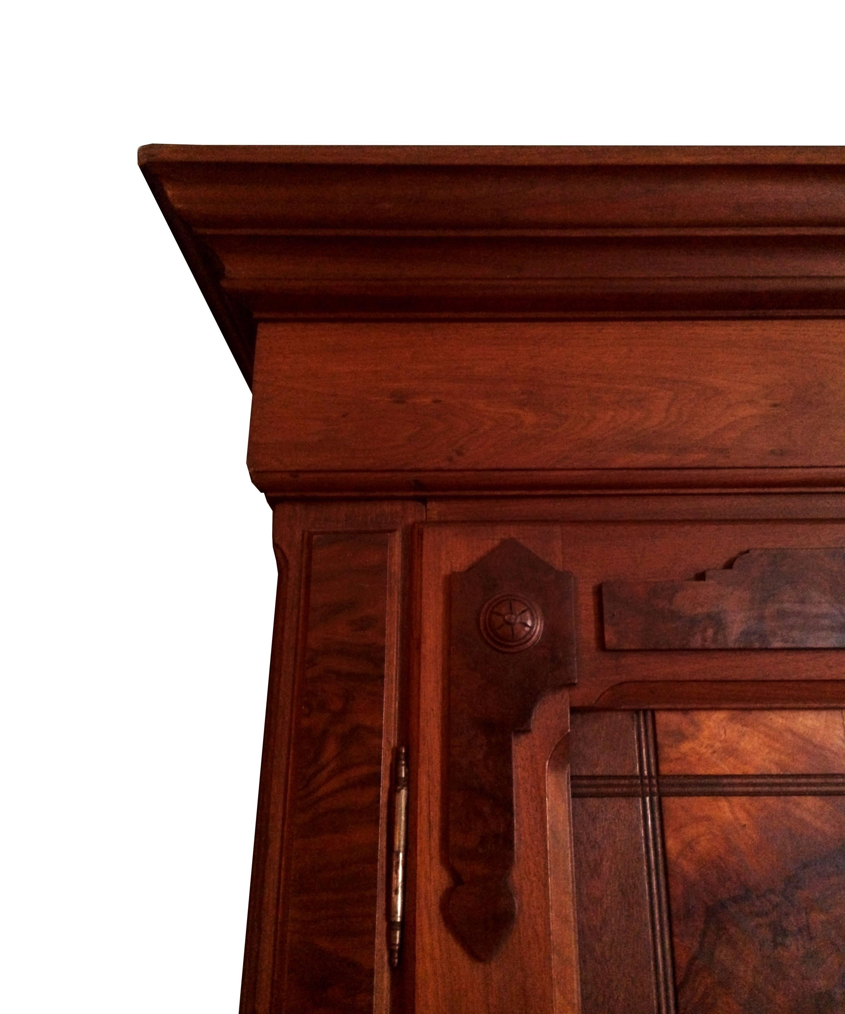 A tall visually astounding walnut and burl veneer wardrobe. The ample ogee cornice rests above powerfully figured burl walnut veneer doors. The doors open to reveal a hate shelf above a chrome-plated hanging rack. The armoire rests on a base
