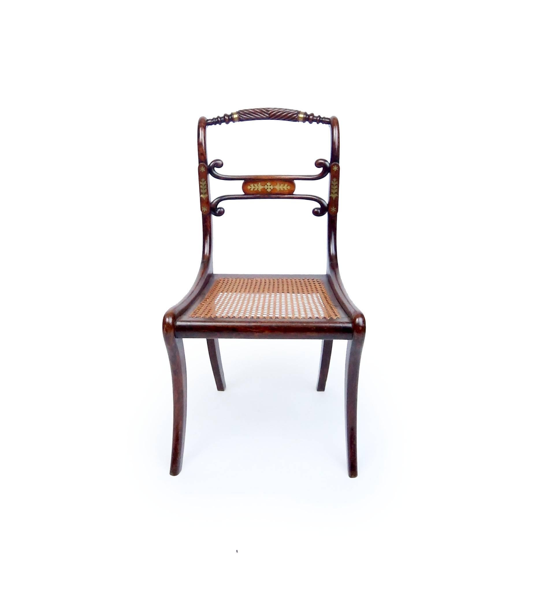 Four fine Geroge III rosewood chairs with inlaid brass details, gadrooned crest rail, and saber legs. Original caned seats, horsehair stuffed button-tufted cushions upholstered in pink silk. One chairs bears a mid-20th century sticker officially