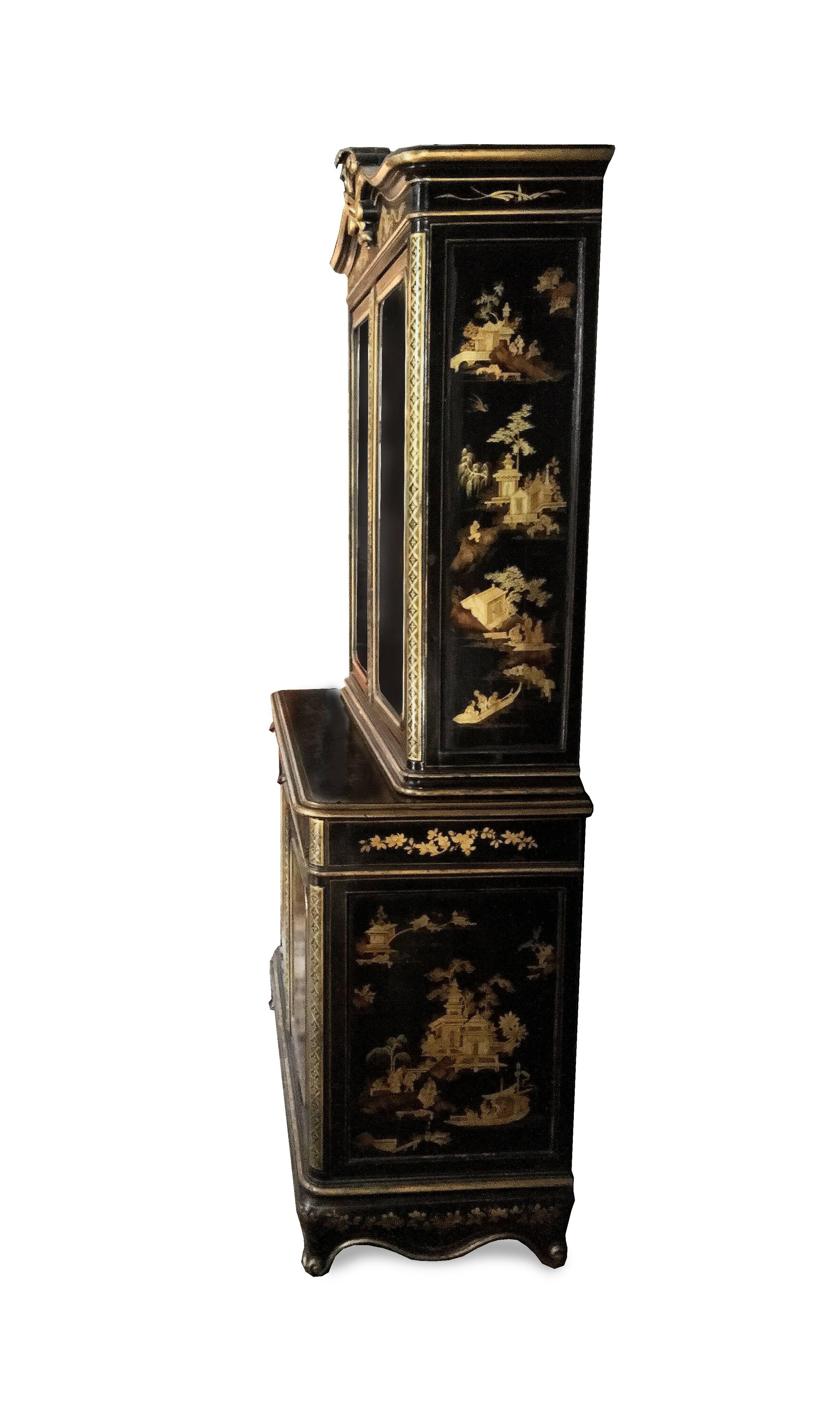 A magnificent lacquered gold and black cabinet covered in exceptionally detailed gilt fretwork and scenery. The glassed upper case features a Baroque scrolled pedimented cornice with volutes and Prince of Wales feathers emerging from a coronet. The