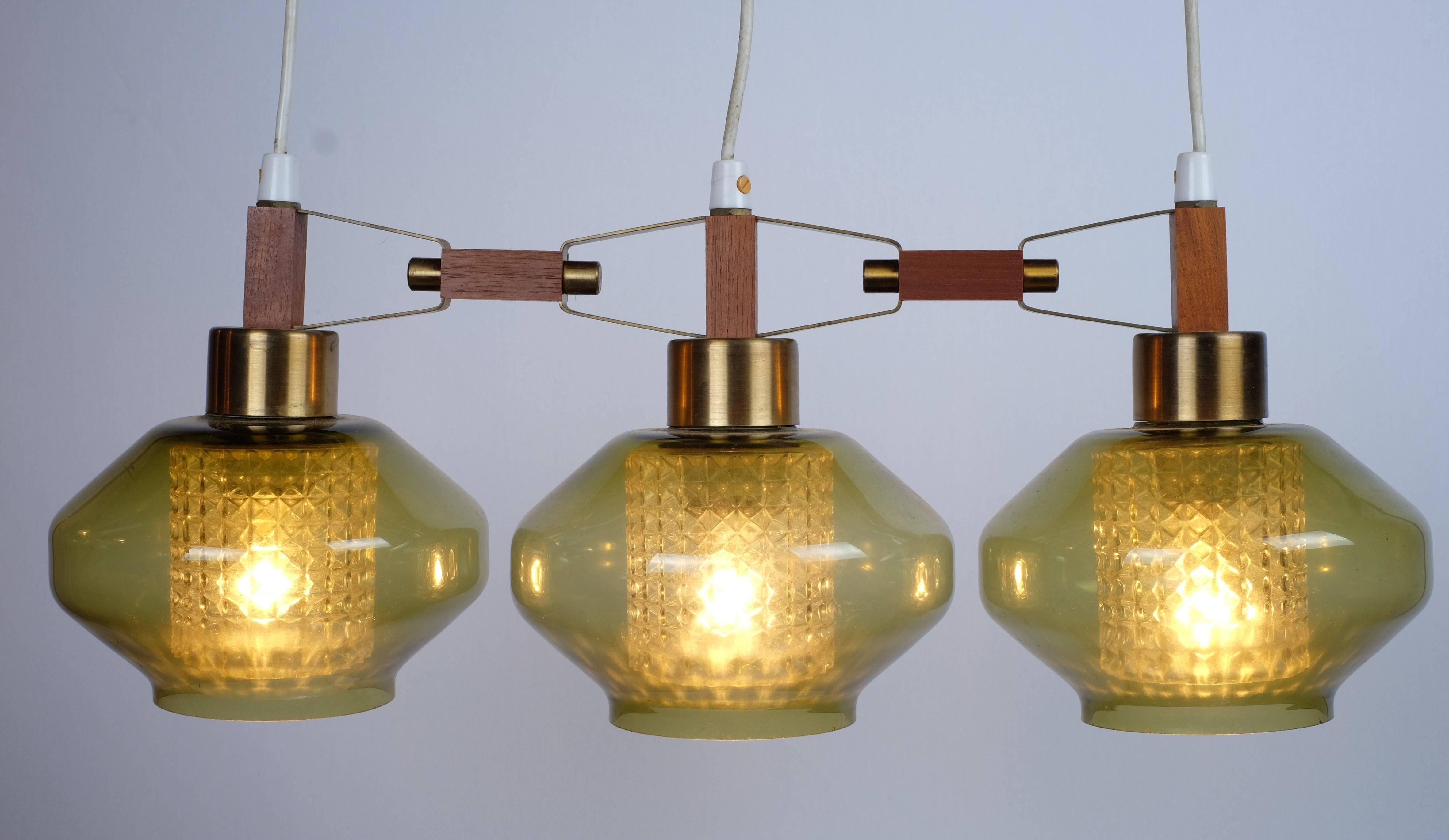 Modernist three-shaded chandelier with top in teak and brass-green glass suspension smoked with crystal inside, attributed to Carl Fagerlund for Orrefors, 1960s. (Rarely seen)

Provides a comfortable light and have a very beautiful