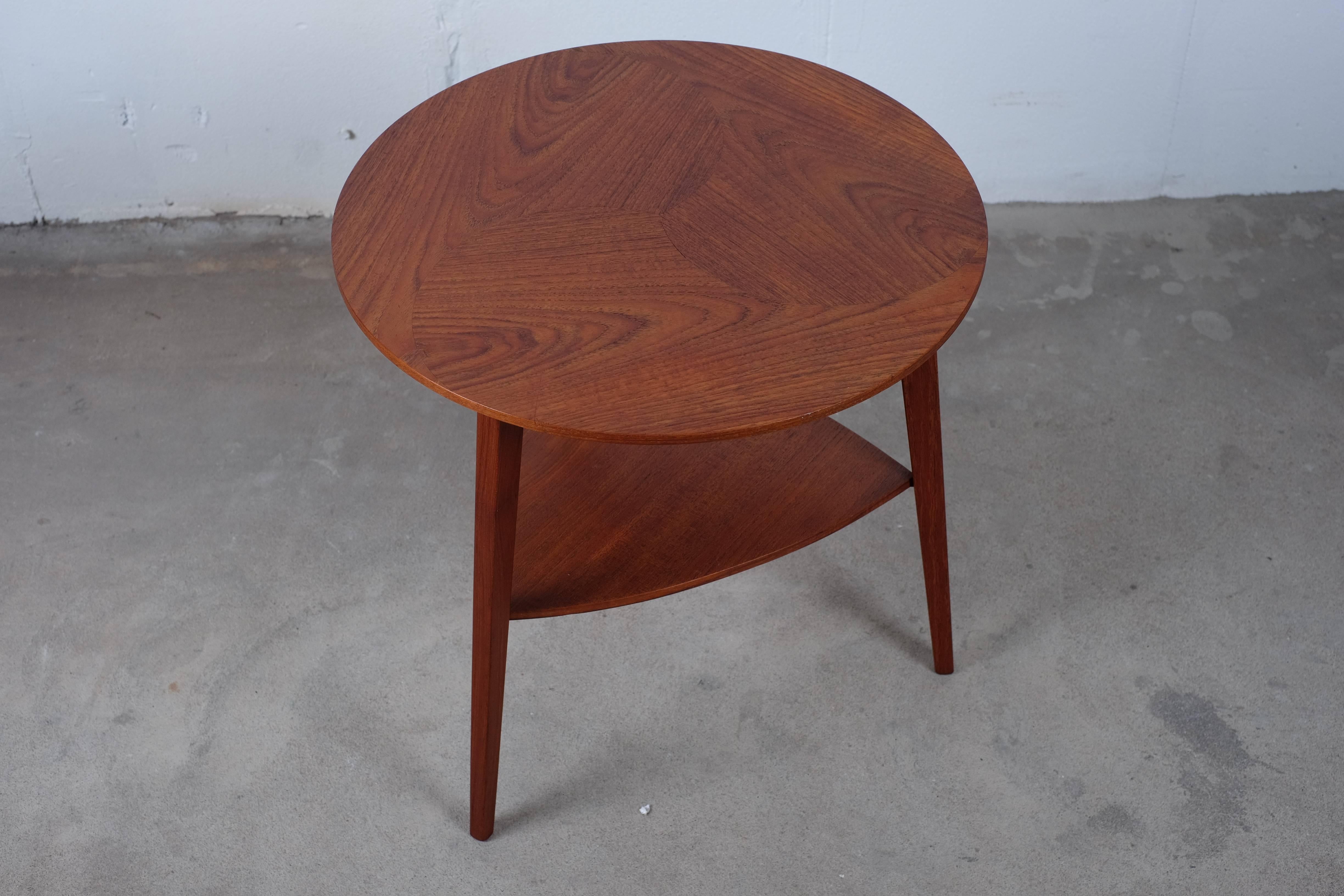 Very elegant three-legged Danish coffee or side table in teak with triangular shelf.

Beautiful top plate where three pieces of veneer are used instead of one. 

The table is from the 1960s and are in very good condition with few age-related