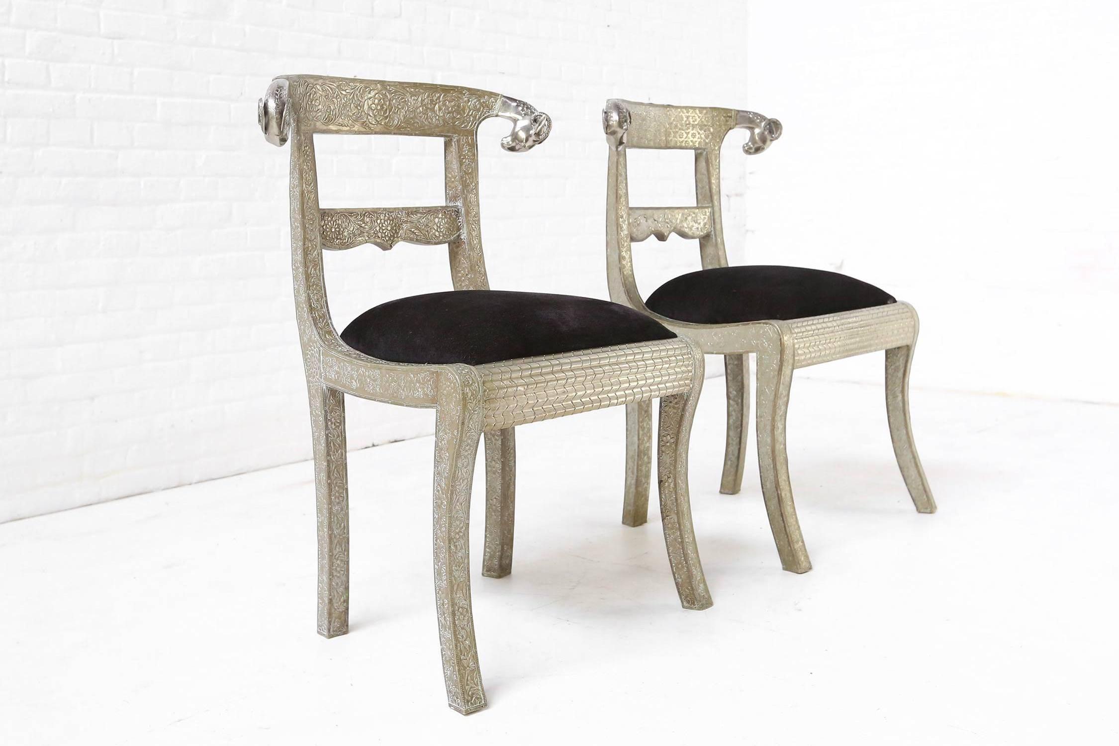 Desirable pair of vintage Anglo-Indian dowry side chairs with ram's head accents. These wonderful chairs feature wooden frames clad in floral embossed silver metal and polished scrolling ram's heads. Seats are upholstered in a black velvet fabric.