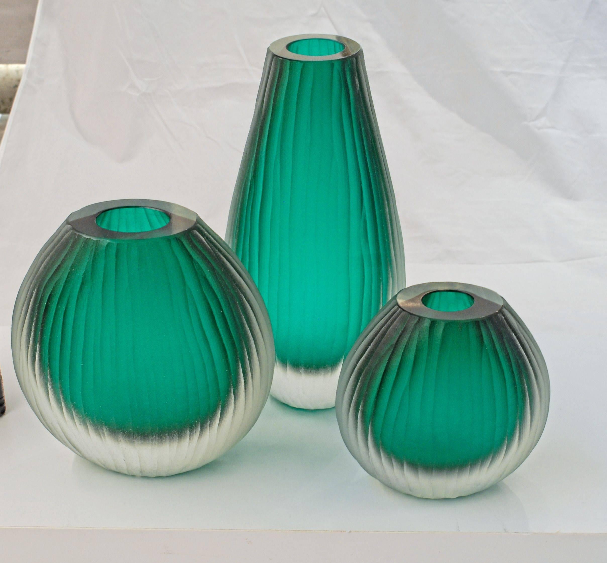 Here a beautiful cluster of three Sommerso vase. The inner color is dark emerald, almost a forest green. The outer glass is a massiccio clear. Each vase is completely finished in battuto.
The play of light is incredible and makes it a great trio for
