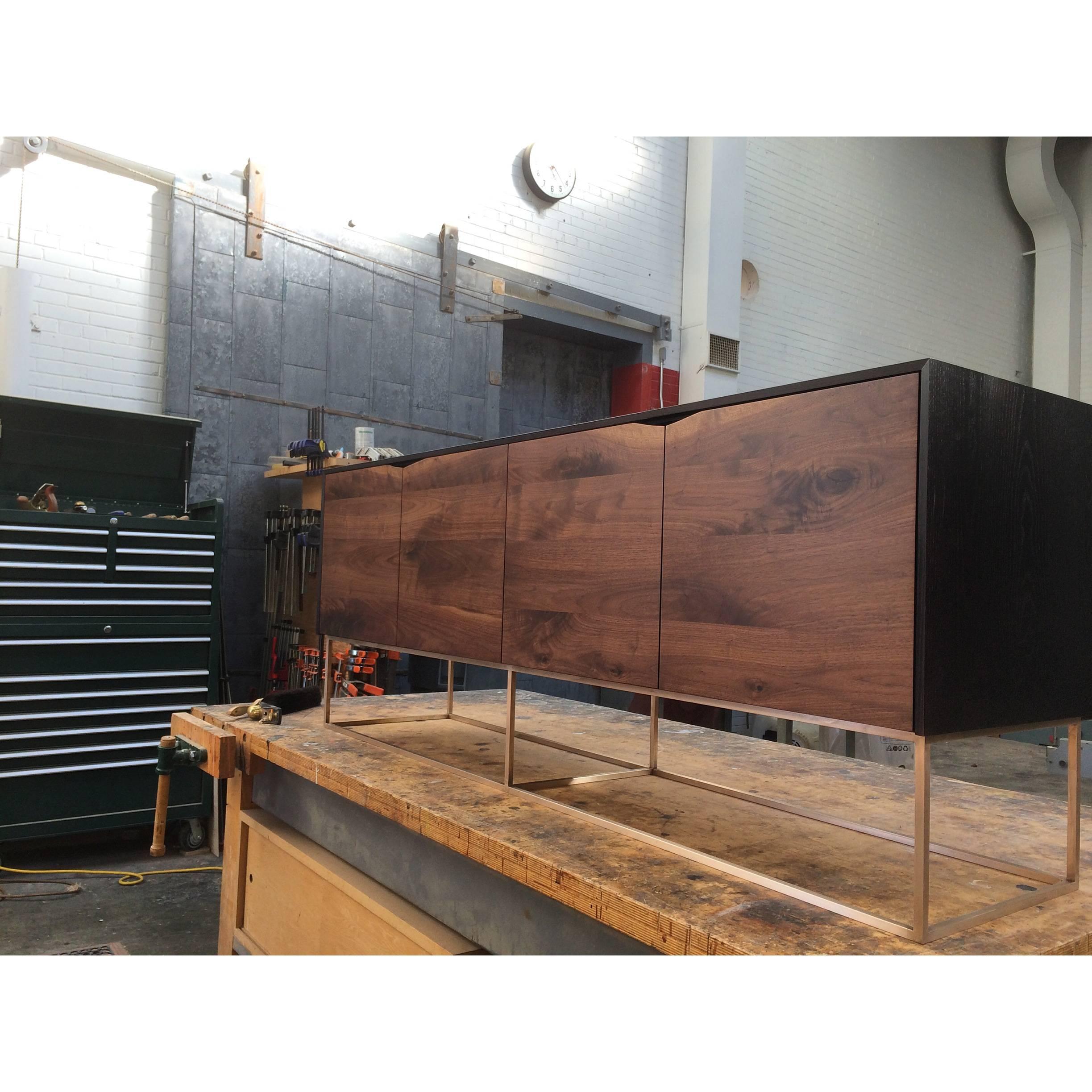 Handcrafted Classic modern credenza of select American hardwoods with a solid bronze base. Ebonized ash cabinet with four walnut soft-closing doors and a solid bronze base. Each compartment has an adjustable shelf. Great for media use or simply as a