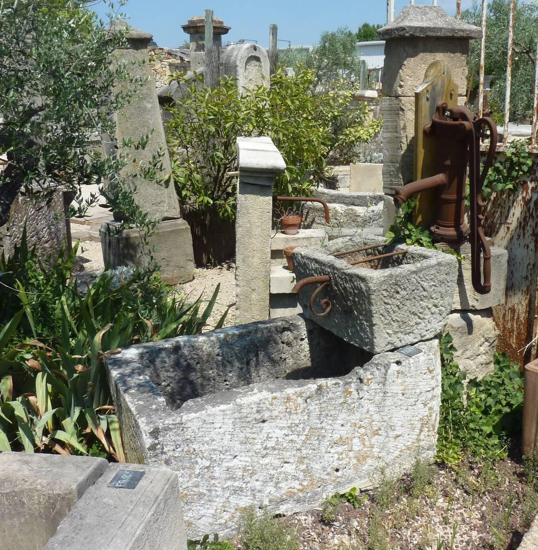 This fountain with two layered monolithic stone basins is topped by an antique cast iron water pump resting on a rustic stone pillar. The highest and smaller basin has two metallic rest-bucket bars (ideal to fill up your watering can). It is drilled