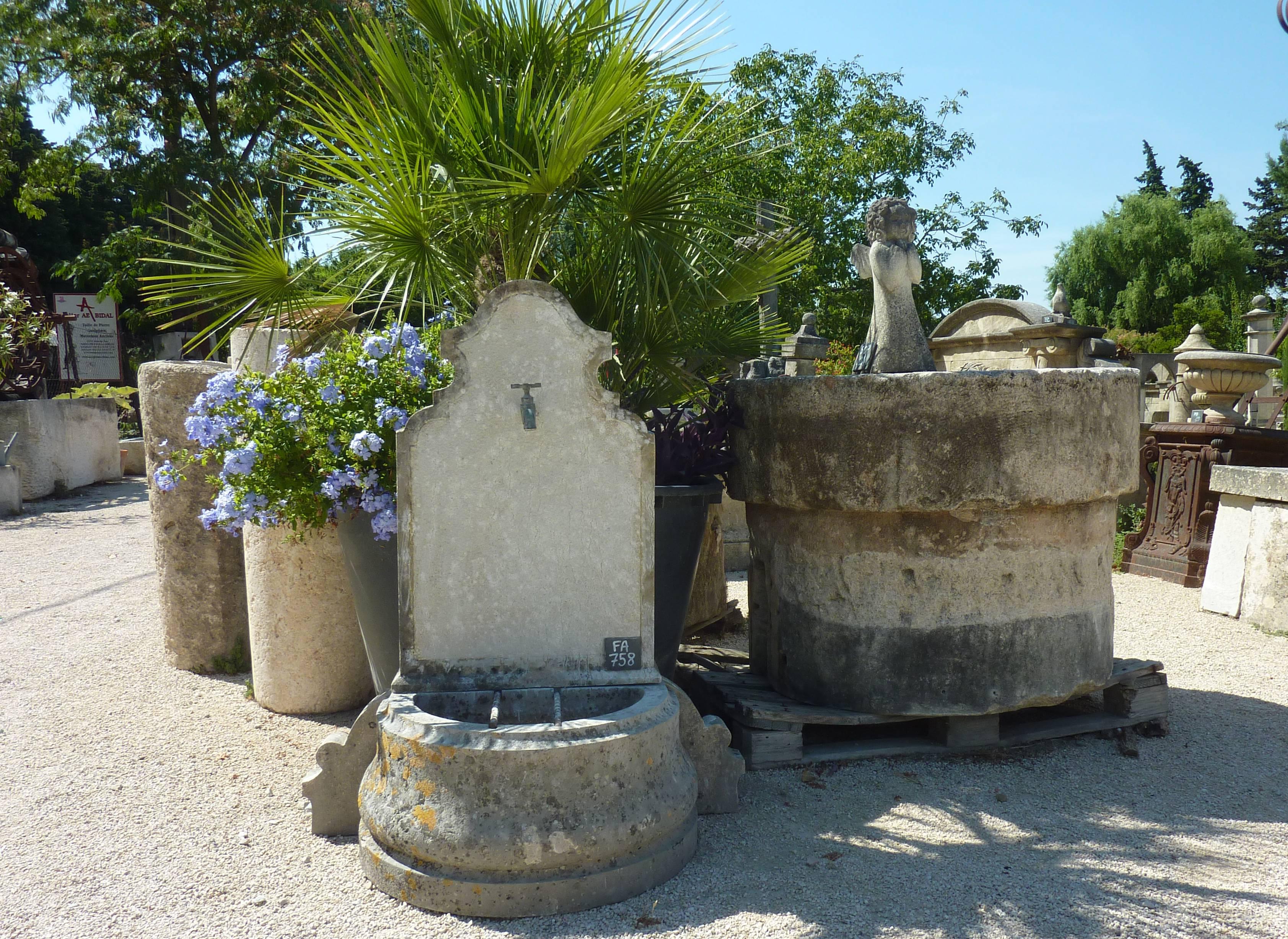 Lovely small garden fountain made of reclaimed materials.

This drinking fountain is composed of a sculpted half-round shaped monolithic basin looking like a trough with two metal rest-bucket bars. The wall piece is also made of an antique