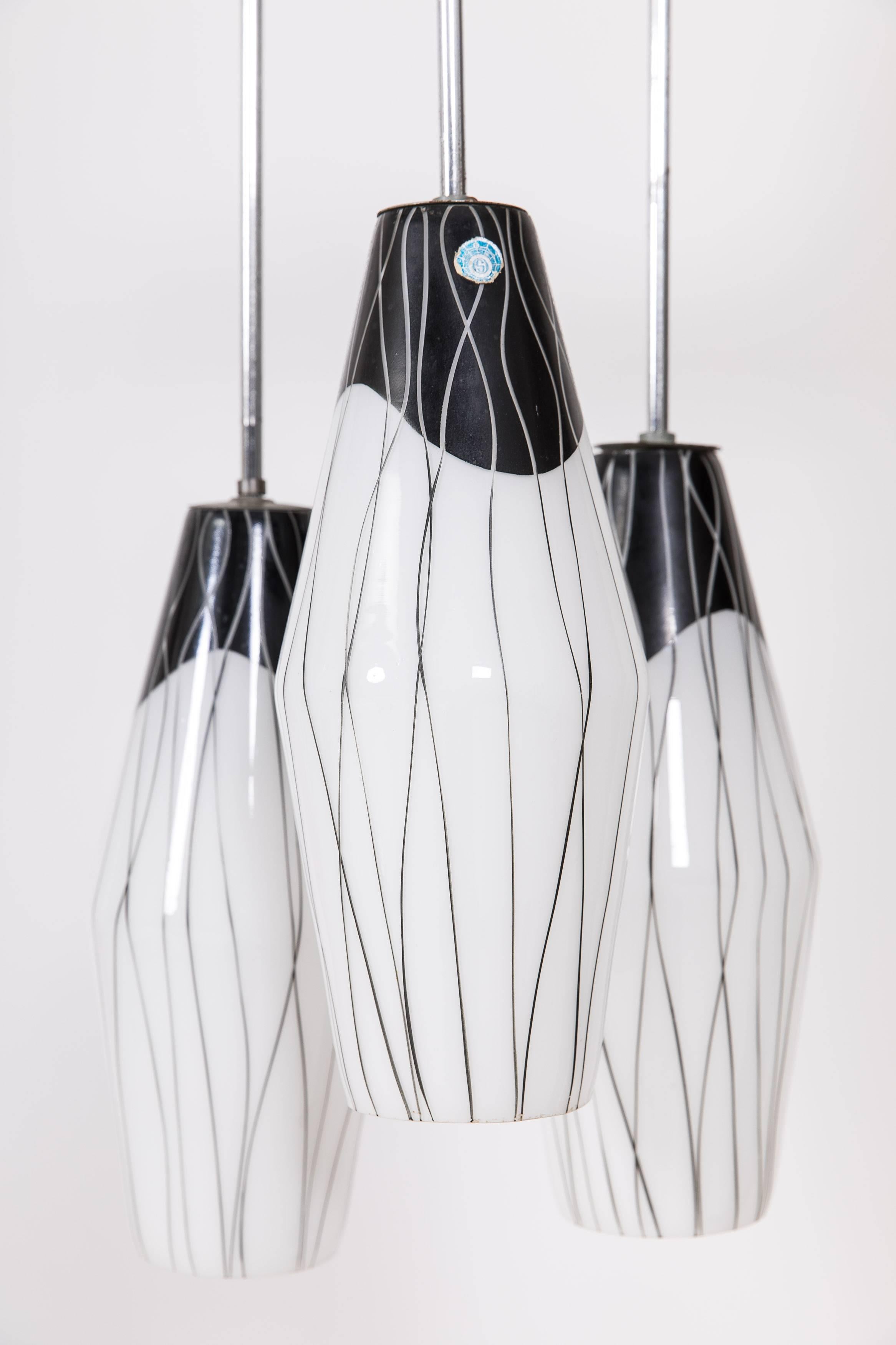 Pendant light made by Zukov lighting factory in the 1960s. Three painted glass cones with a height of 35cm and a diameter of 9cm. The glass cones are mounted on a chrome frame with a total height of 70cm.

This pendant light is suitable for E27