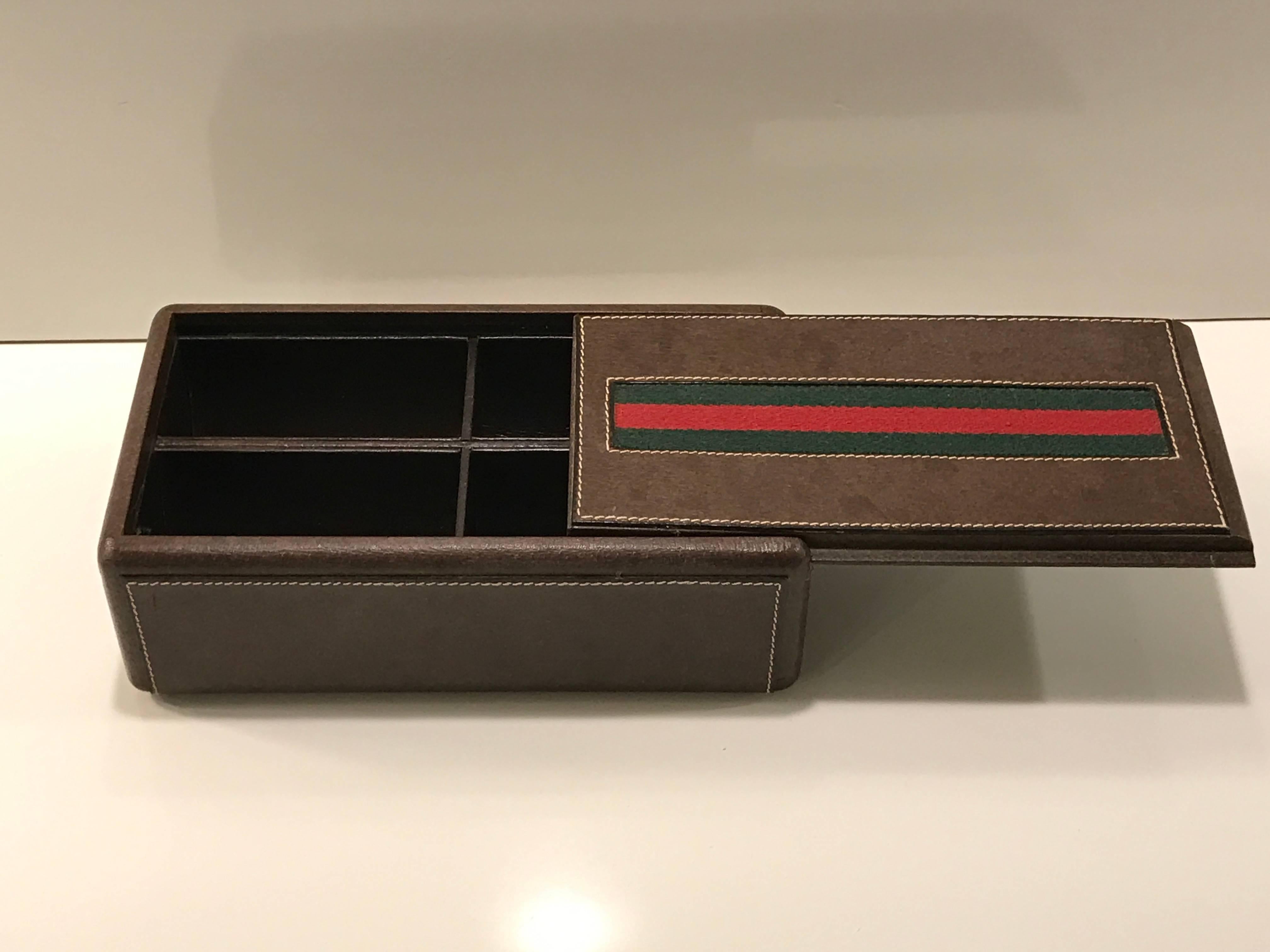 Gucci leather mens jewelry or watch box with divided interior, of rectangular form with inset signature green and red stripe logo, on a stitched calfskin box. The sliding lid reveals four (4" x 1 3/4" W x 2" D) rounded compartments