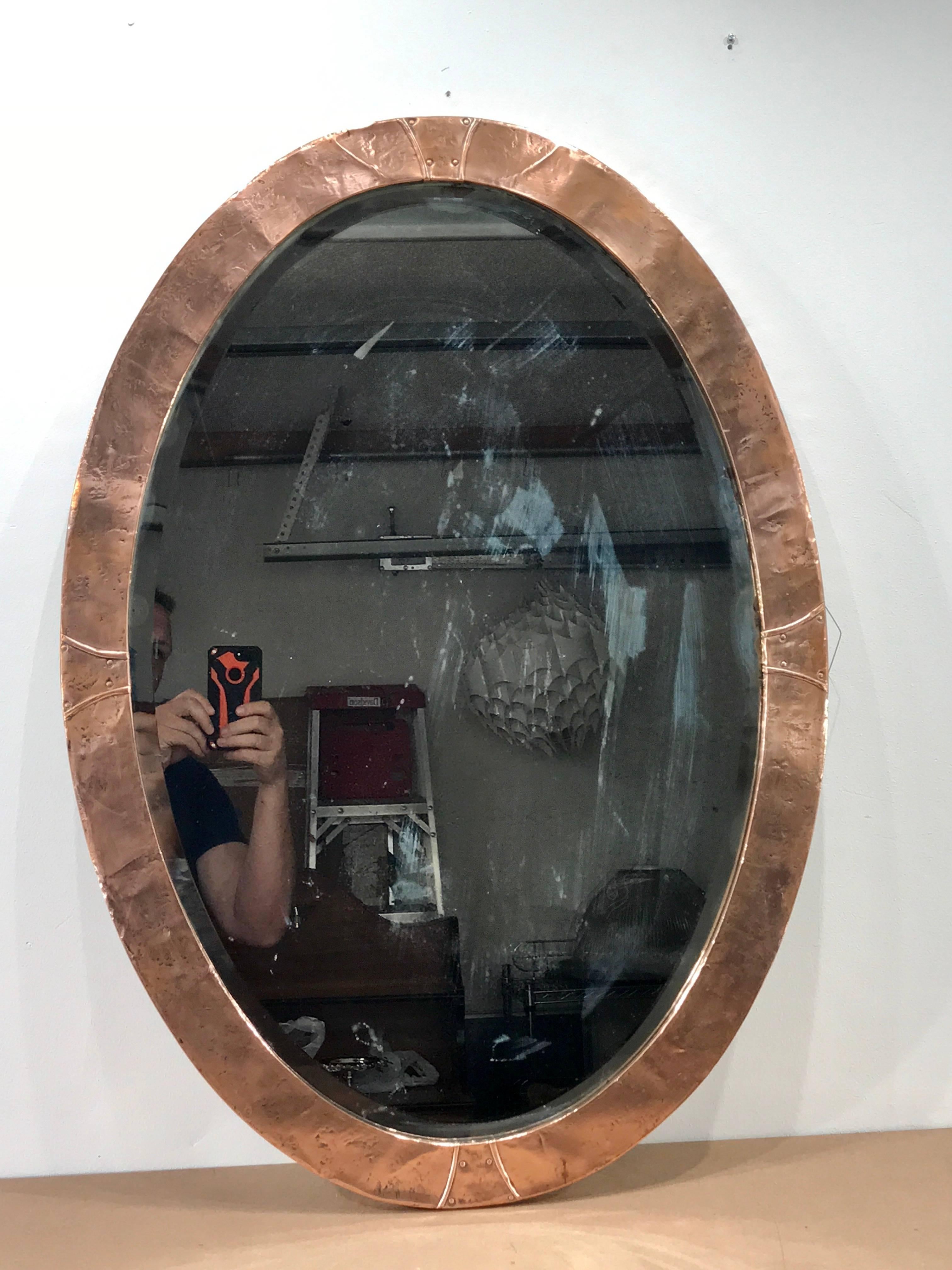Art & Crafts hammered copper wall mirror, attributed to the Glasgow school, of oval form with hand-forged nearly seamless copper frame with inset bevelled mirror that measures 29.5
