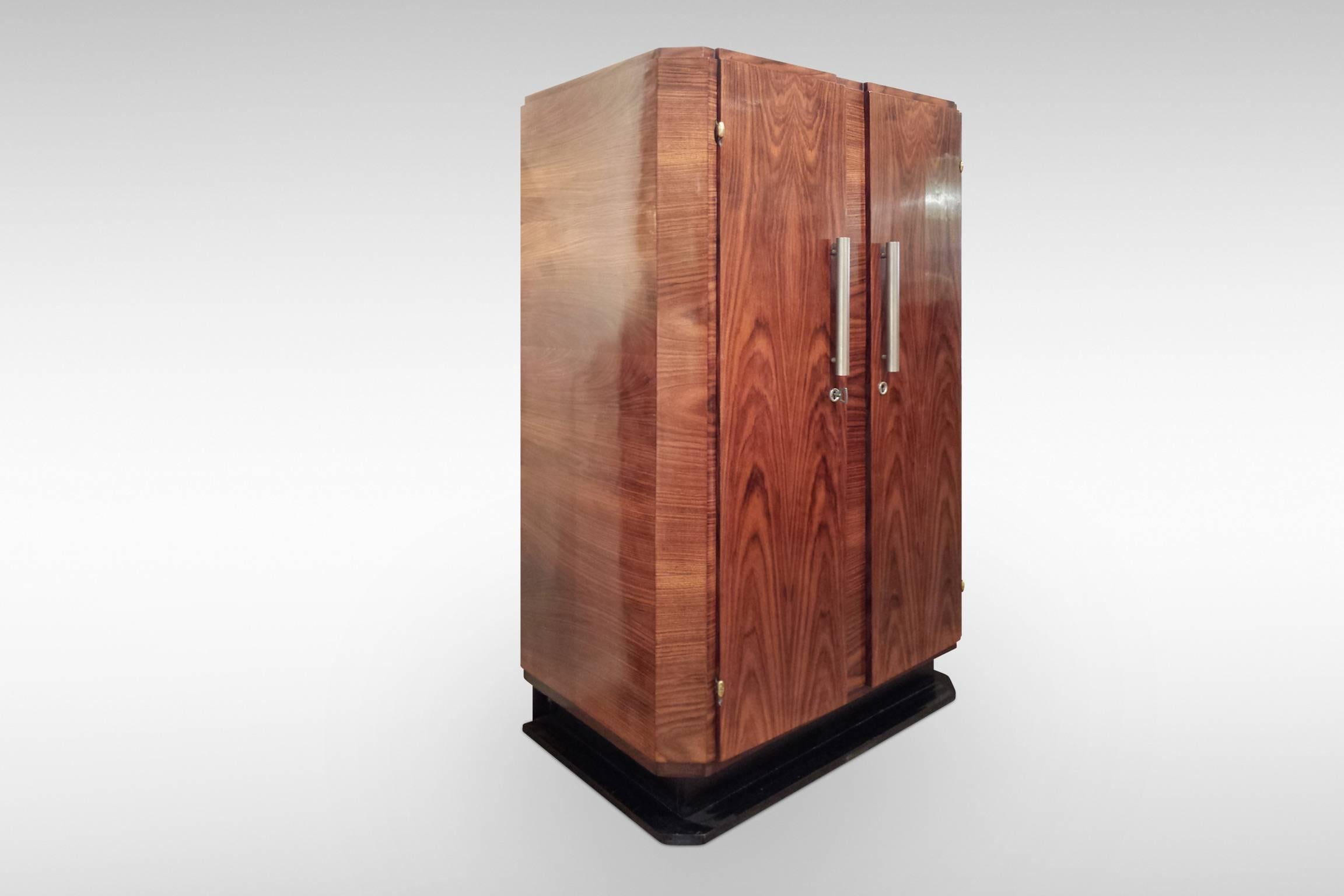 A stylish Art Deco storage cabinet with double doors enclosing two adjustable shelves. The strikingly figured veneers are probably rosewood complimented by an ebonised plinth. Modernist chrome handles, escutcheons and key, circa 1930s-1950s.