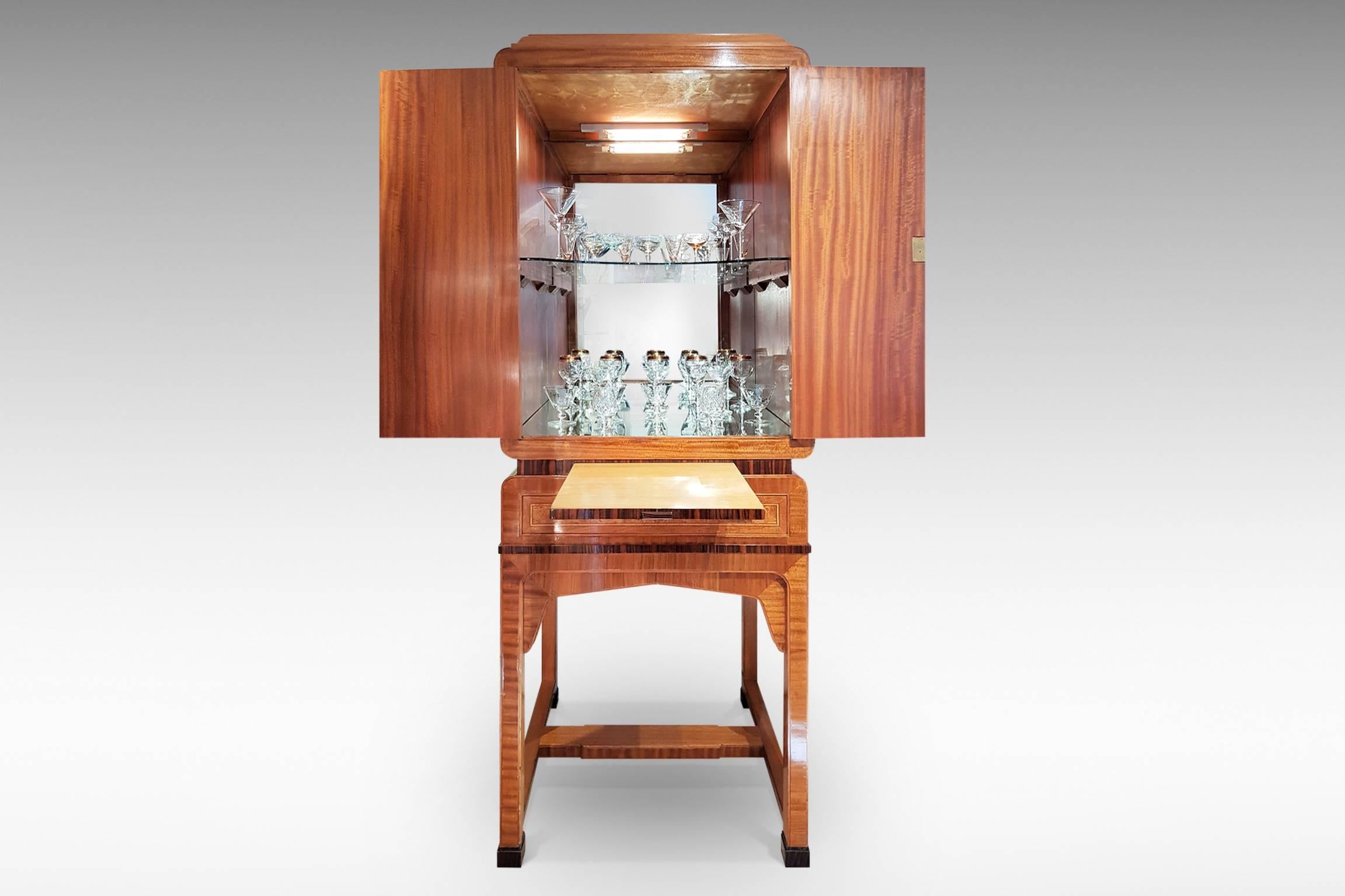 This a superb quality Art Deco cocktail cabinet with veneers and banding in burr walnut, satinwood, mahogany, Macassar ebony and others. It has a mirrored and illuminated interior with glass shelf, together with a pull-out shelf and drawer below.