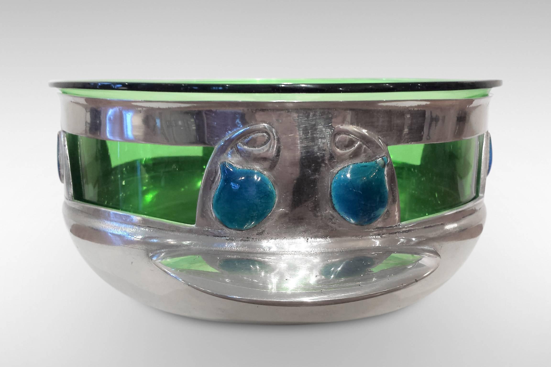 This rose bowl is in a striking design by Archibald Knox for the Liberty & Co 'Tudric' Pewter range. It is enhanced by plaques of blue/green enamel and has a green glass liner.
Marked 'Tudric 0320', the design was registered at The Patents,