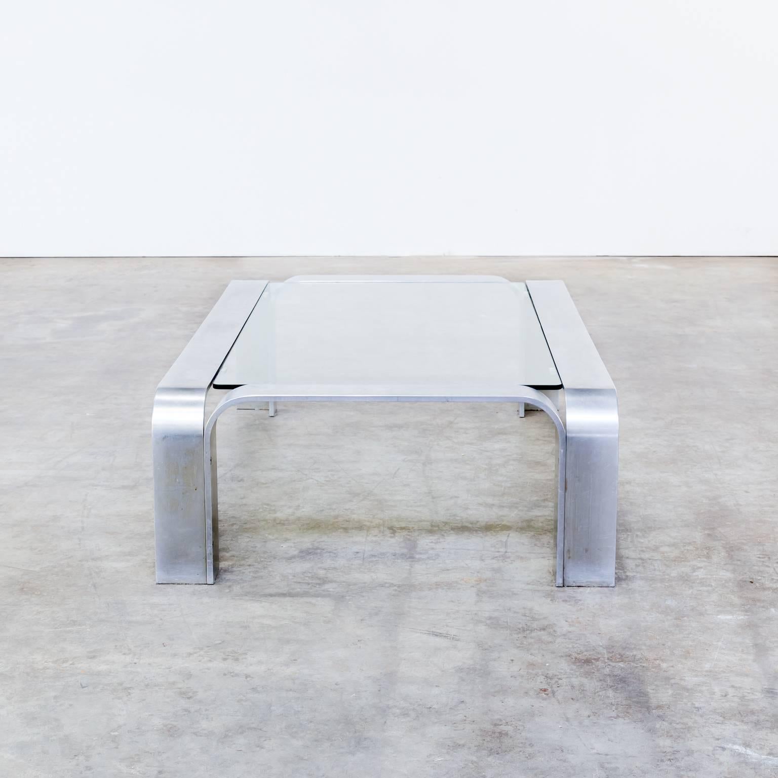 1990s coffee table in aluminium and glass. Rectangular table with glass top. The aluminium frame consist of four arches. Aluminium strips with rounded edges and nice patina. One chip of the glass and small usage scratches in it. Dimensions: 116cm W