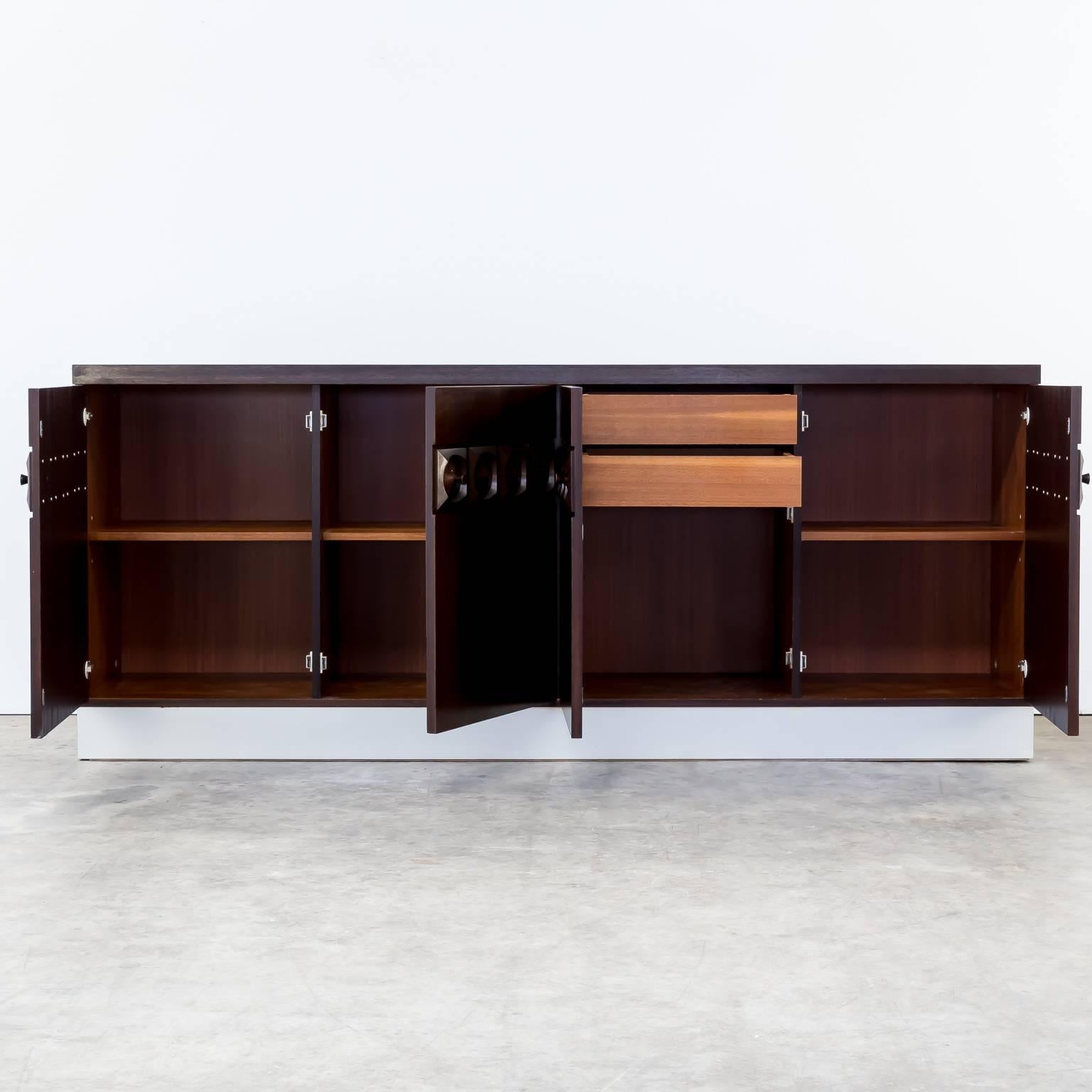 1970s Belgian Brutalist credenza sideboard attributed ‘de Coene’. Red/brown teak, silver plint. Original condition, wear consistant with age and use. Dimensions: 220cm (W) x 50cm (D) x 91.5cm (H).