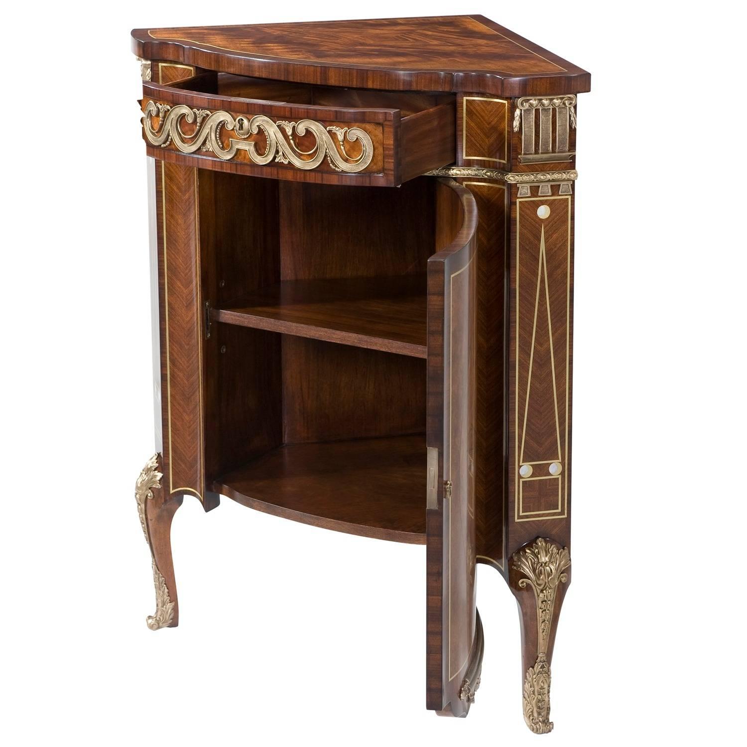 A mahogany, rosewood, laurel burl and pollard oak burl, brass and mother-of-pearl inlaid corner cabinet, the brass-mounted frieze drawer above a musical trophy inlaid cabinet door enclosing an adjustable shelf, on cabriole legs. The original Louis