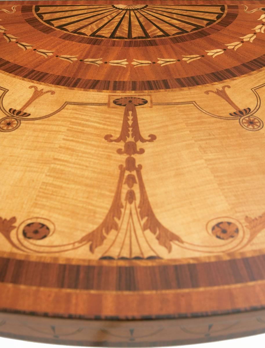 An intricate sycamore and specimen marquetry console table in the manner of Robert Adam. With fan inlaid bowfront top above a floral swag inlaid frieze, on square tapering legs decorated with trailing bell-flowers. The original circa 1770,