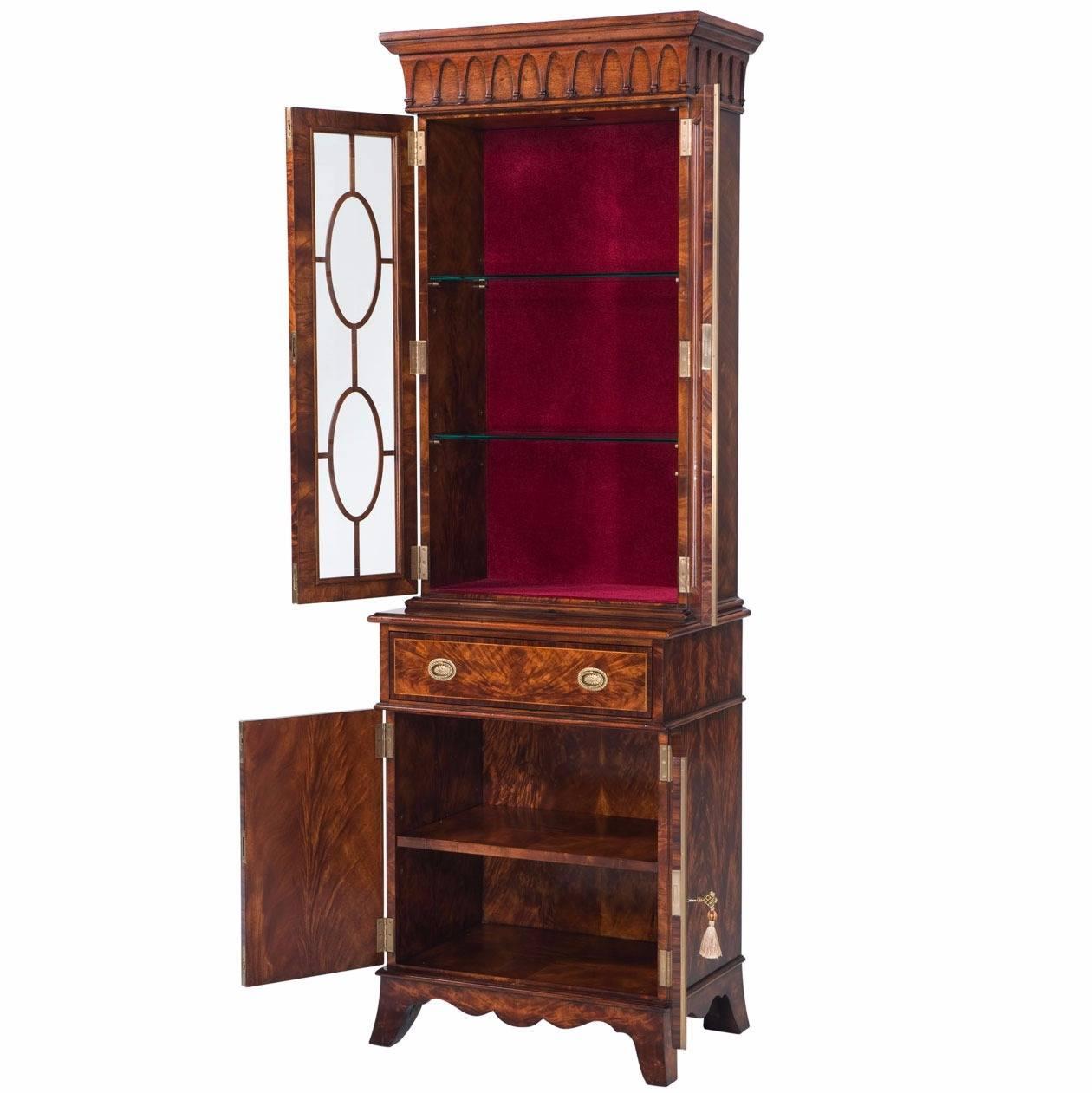 A narrow George III Sheraton style mahogany library bookcase. The upper section has a moulded cornice above an icicle frieze over two glazed doors with oval astragals enclosing a velvet lined interior with glass shelves and touch lights. The cabinet