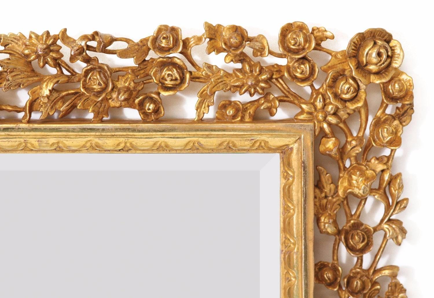 Giltwood mirror with rectangular bevelled glass plate framed with an intricately detailed repeating floral design, hand-carved in a mahogany and water gilded in 23¾ carat gold leaf. Toned with a ‘bright and matte’ effect, the highlighted areas
