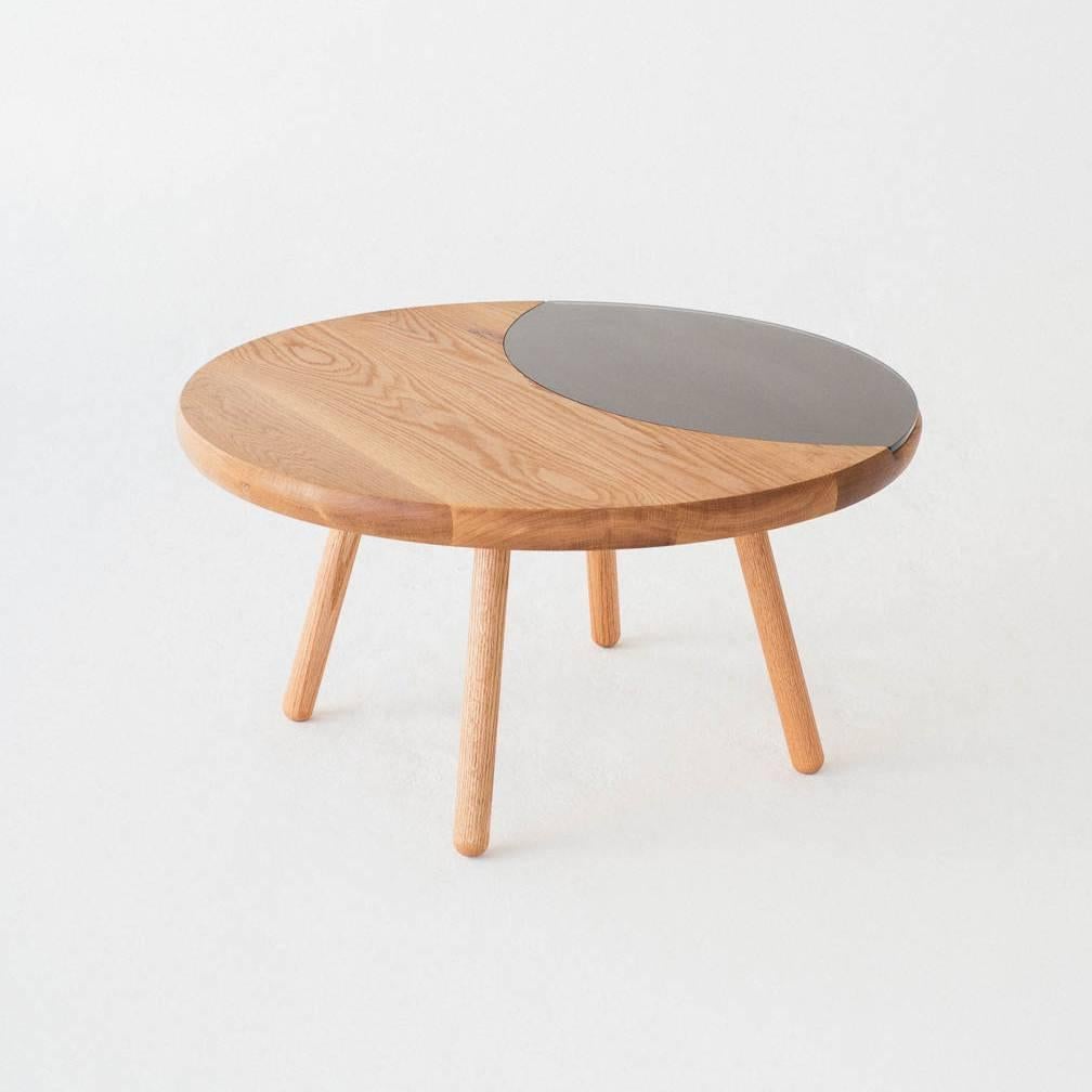 The Dibbet coffee table is a minimalist, round table with a glass lens-shaped insert recessed into the top. A comfortable and contemporary living room centerpiece or side table, the hard insert is duly Apt to help you take down a note or place a