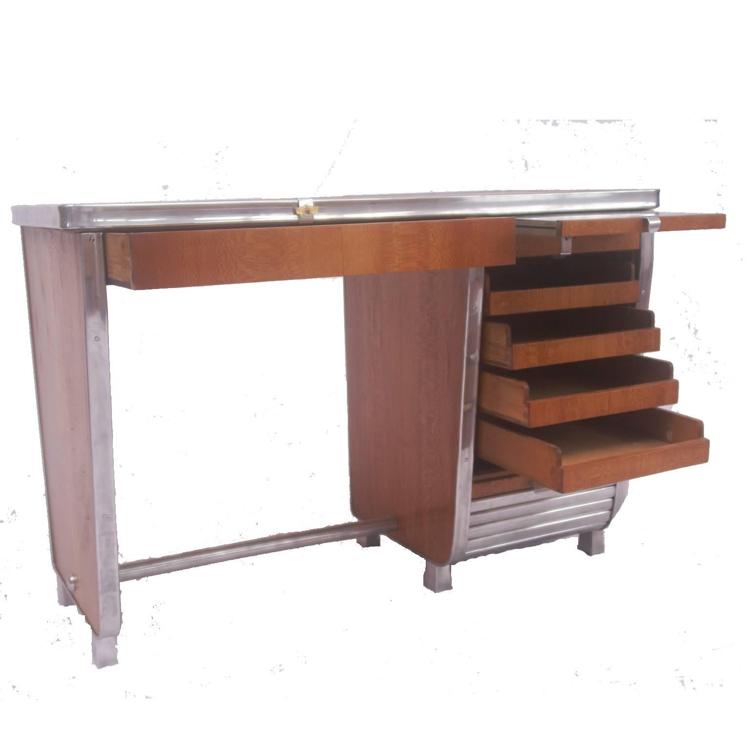 Small Art Deco desk with aluminium mounts and slatted aluminium roller front. Quarter veneered top and matched veneers throughout. The roller shutter covers four drawers, with one other drawer to front, Aluminium slide above shutter. Badge of French