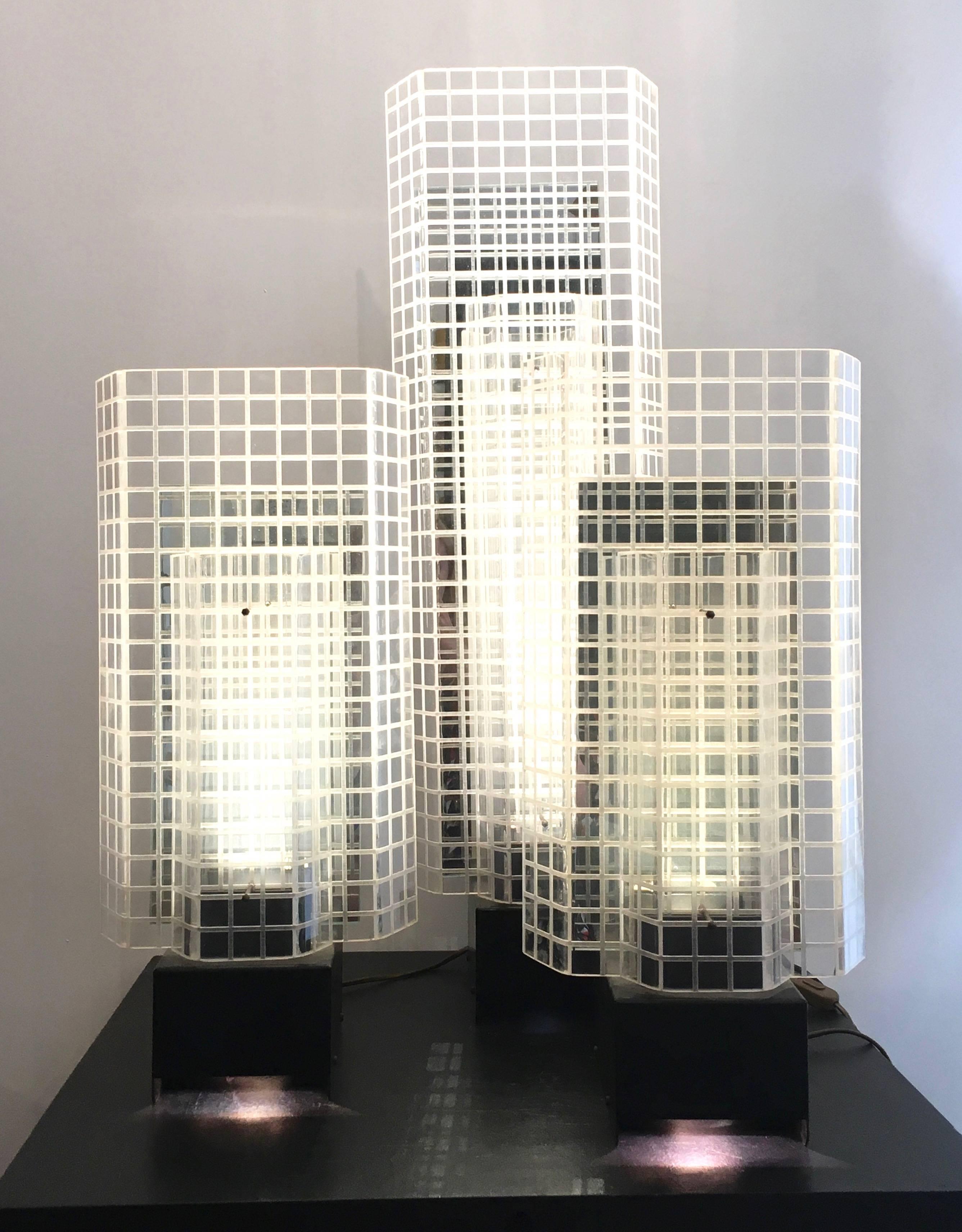 A set of three 1980s design Skyscrapers table lamps with a mirror slab reflecting the bulb cover in turned and Chiseled plexiglass in a building shape on a quadrangular base in blackened metal.

Dimensions: 
H 86 cm, D 21 cm, W 26 cm
H 56 cm, D