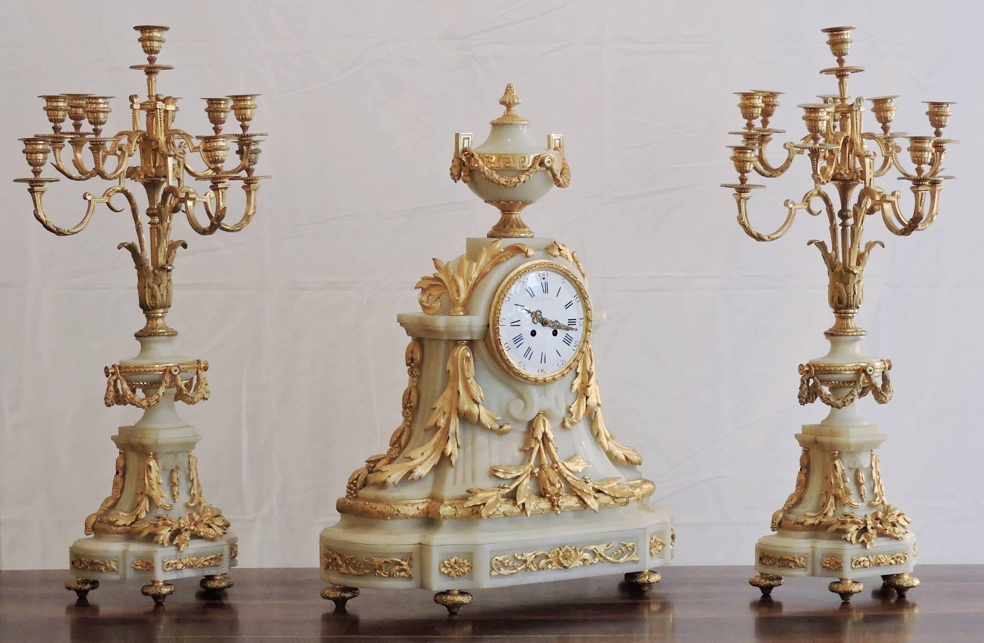 Comprising a clock and a pair of ten-light candelabra, this is an impressive piece of 19th century taste and style by Raingo Brothers (Raingo Frères). 

Above the French mantel clock, a classic from of urn is garnished with Greek fret and a laurel