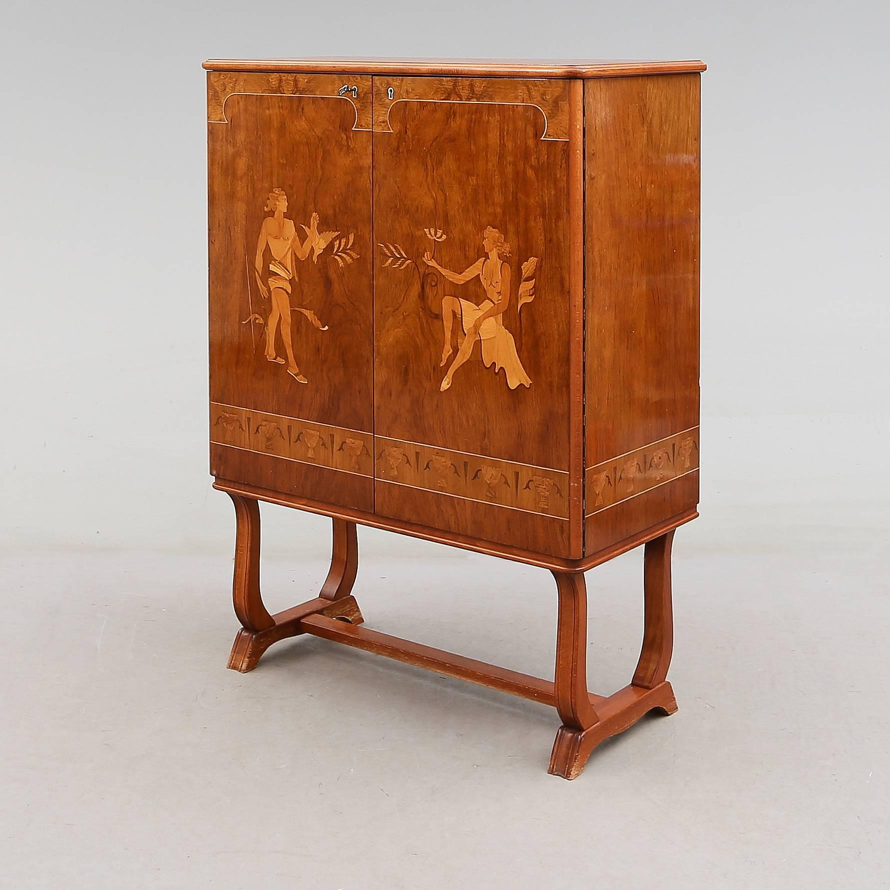 Intricately inlaid Swedish Grace (streamlined classicism circa 1920-1940) storage cabinet with allegorical male and female friezes. Rendered in walnut, birch, Carpathian elm and rosewood. 

Interior consists of removable or adjustable shelves and