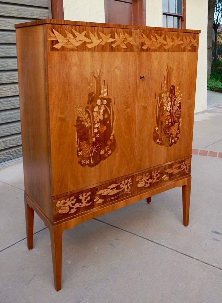 Swedish Mid-Century inlaid storage cabinet by Reiners Möbler with flora and fauna motifs, circa 1950. Rendered in birch wood and rosewood with mixed wood marquetry. This piece has just been beautifully restored by our craftsmen.