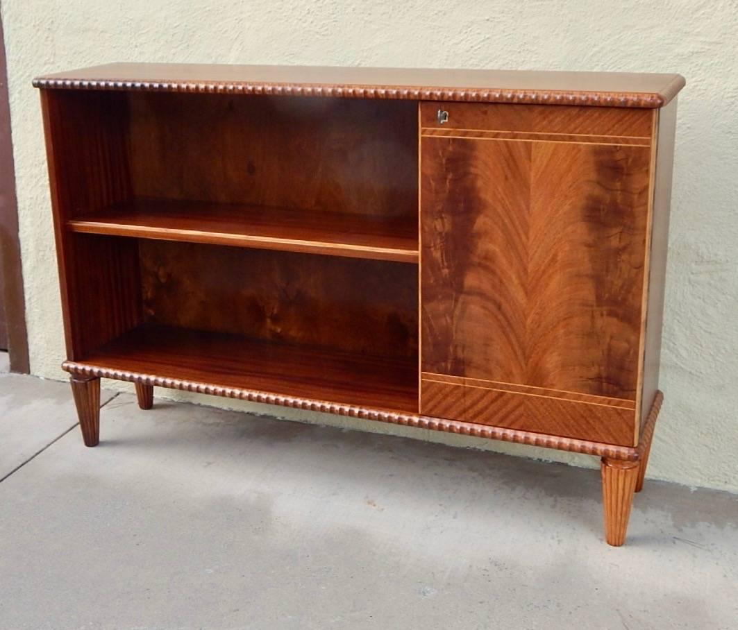 Swedish mid-20th century bookcase rendered in mahogany with highly figured bookmatched Honduran mahogany front. There is one adjustable/removable shelf for the exterior. There are two shelves for the interior. Completely restored by our craftsmen to