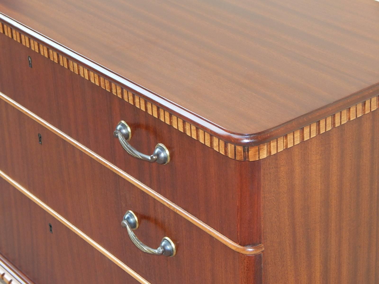 Swedish 1940s moderne chest of drawers. Rendered in birch and flame mahogany. All original classically inspired hardware. Restored by our craftsmen to its original luster.