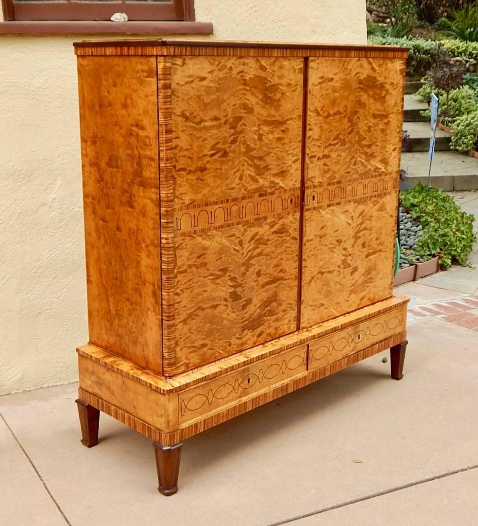 Swedish art deco storage cabinet rendered in highly figured golden flame birch wood. 
With stained birch feet and ebony inlay. Beautifully restored by our woodworkers.  Sweden circa 1930s.