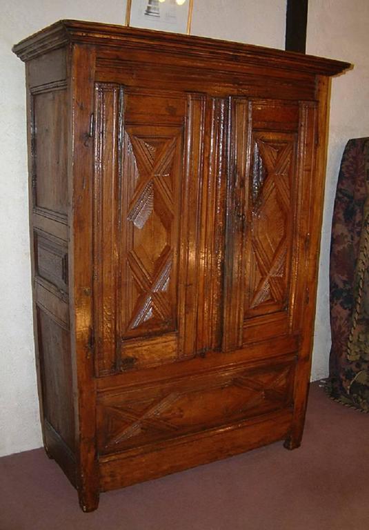 A late 17th century, Louis XIV period oak and walnut armoire of small size dating to, circa 1680. The Moulded cornice above a pair of doors on iron pin hinges with thick carved geometric panels containing a shelved interior. Below, a thick carved
