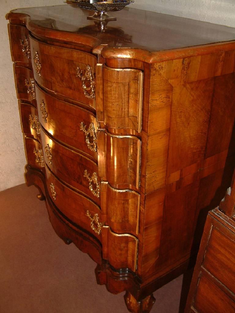 A large Danish/South German walnut commode Altona dating from circa 1750 of shaped Arc en Arbalette form and with parcel-gilt decorative highlights. The shaped crossbanded top with gilded moulded edge above four long shaped, crossbanded drawers,